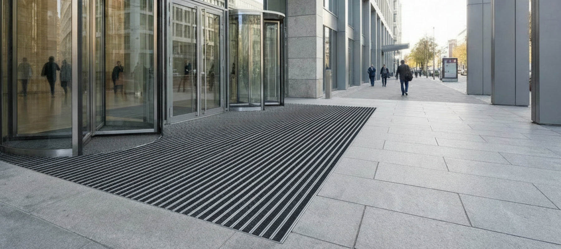 Steinfliesen mit eingelassener Eingangsmatte aus Aluminium mit Ripseinlage vor Geschäftasgebäude.