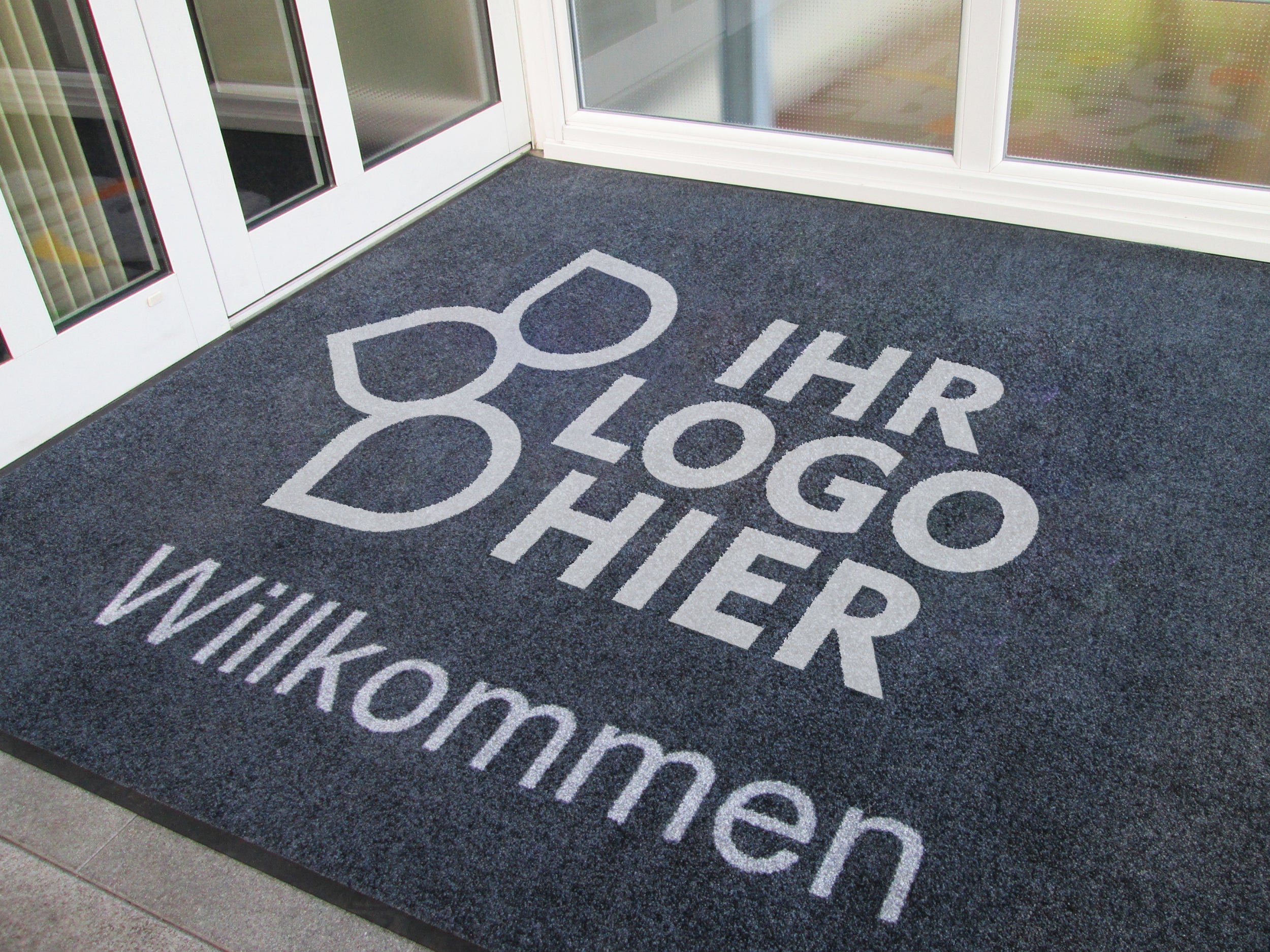 Individualisierbare Logomatte in einer Lobby liegend mit dem Schriftzug: Ihr Logo hier und Herzlich Willkommen