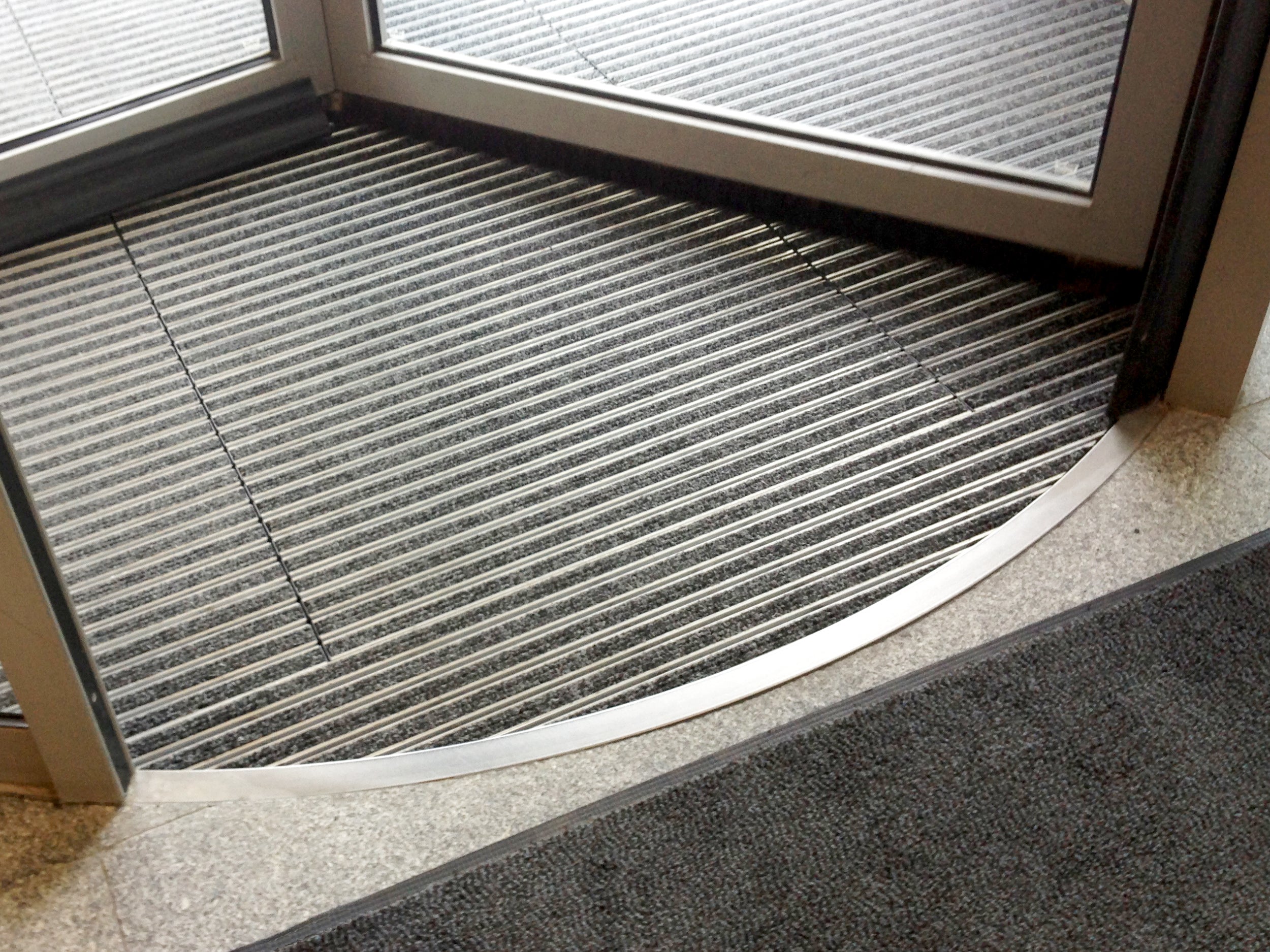 Aluprofilmatte mit schwarzer Ripseinlage liegt als Sonderform in rund in Drehtür – der Rand wird von einer Metallleiste abgedeckt