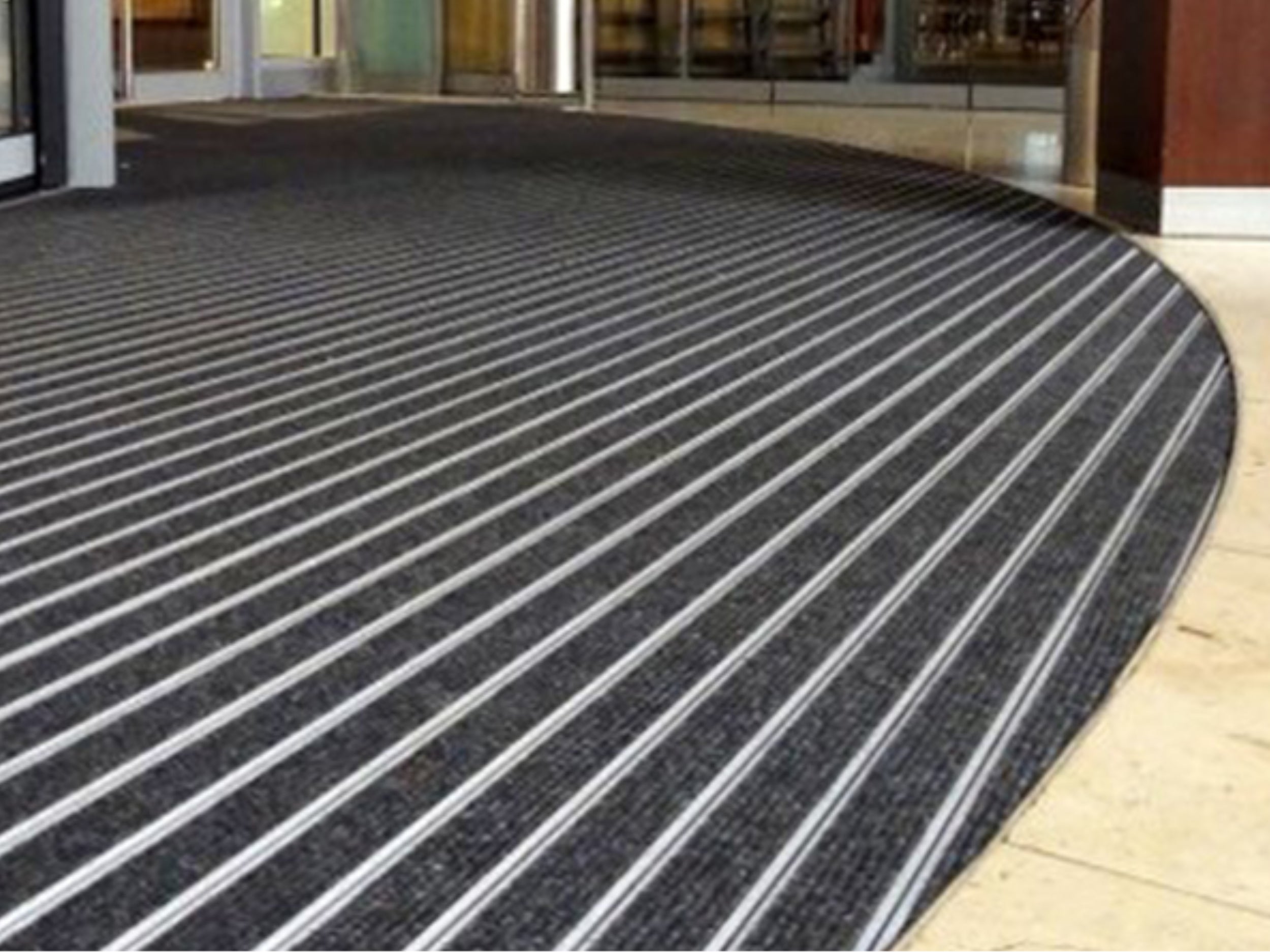 Drehtür mit runder Aluprofilmatte mit schwarzem Materialeinsatz, die in den Fliesenboden eingelassen ist