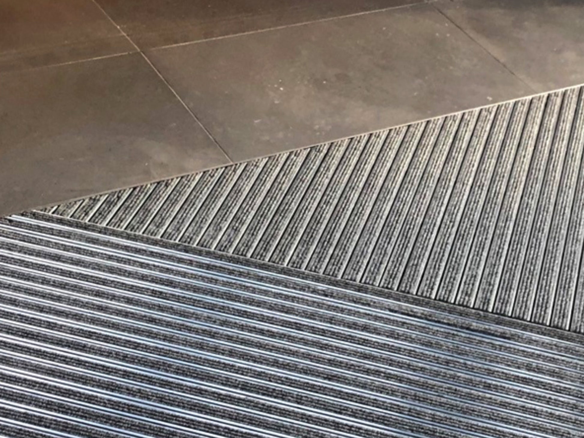 Aluprofilmatte in schräger Form in grau ist in einem Fliesenboden eingelassen