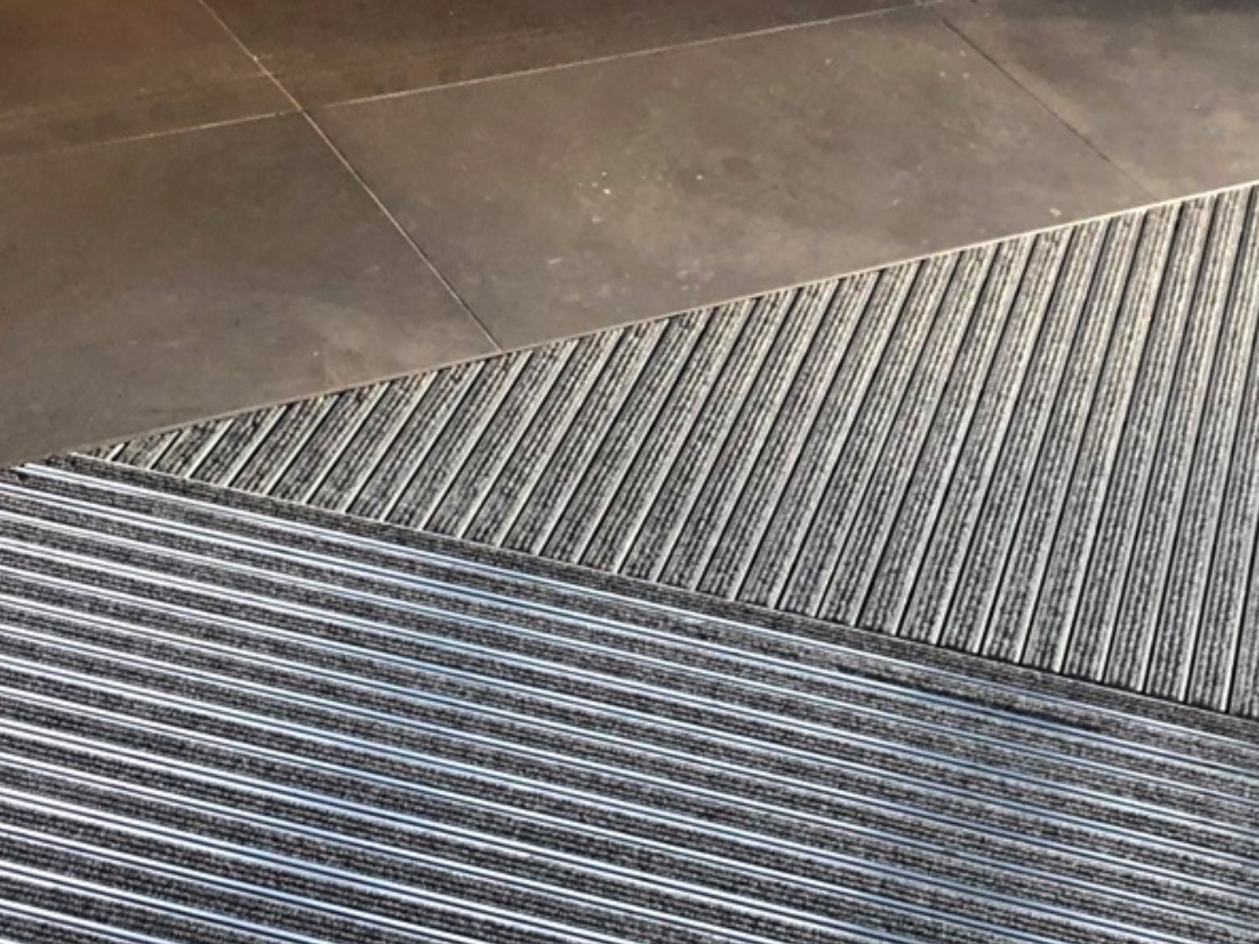 Aluprofilmatte in schräger Form in grau ist in einem Fliesenboden eingelassen