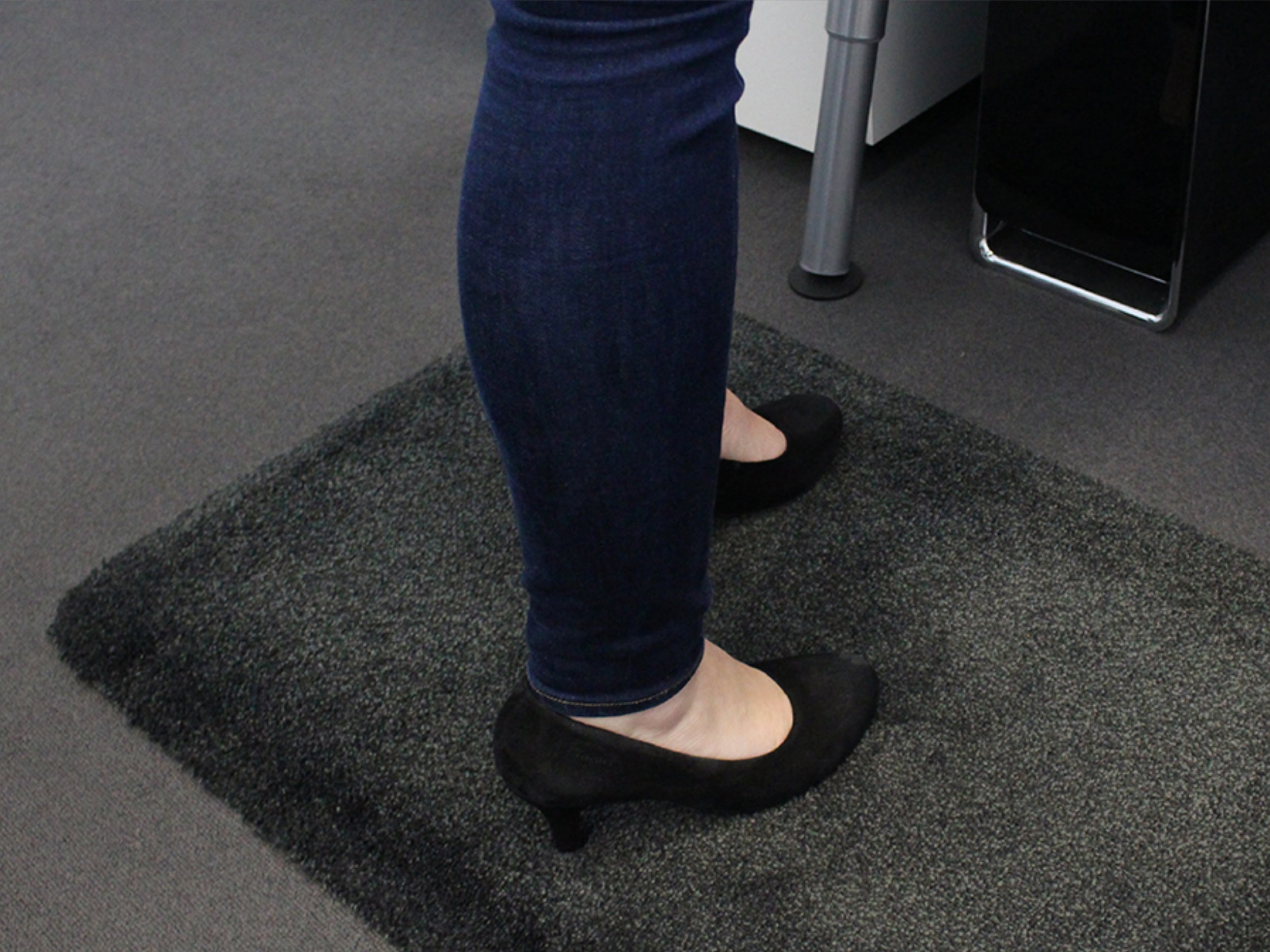 Frau mit Jeans steht auf ergonomischer Arbeitsplatzmatte mit Teppichoberfläche