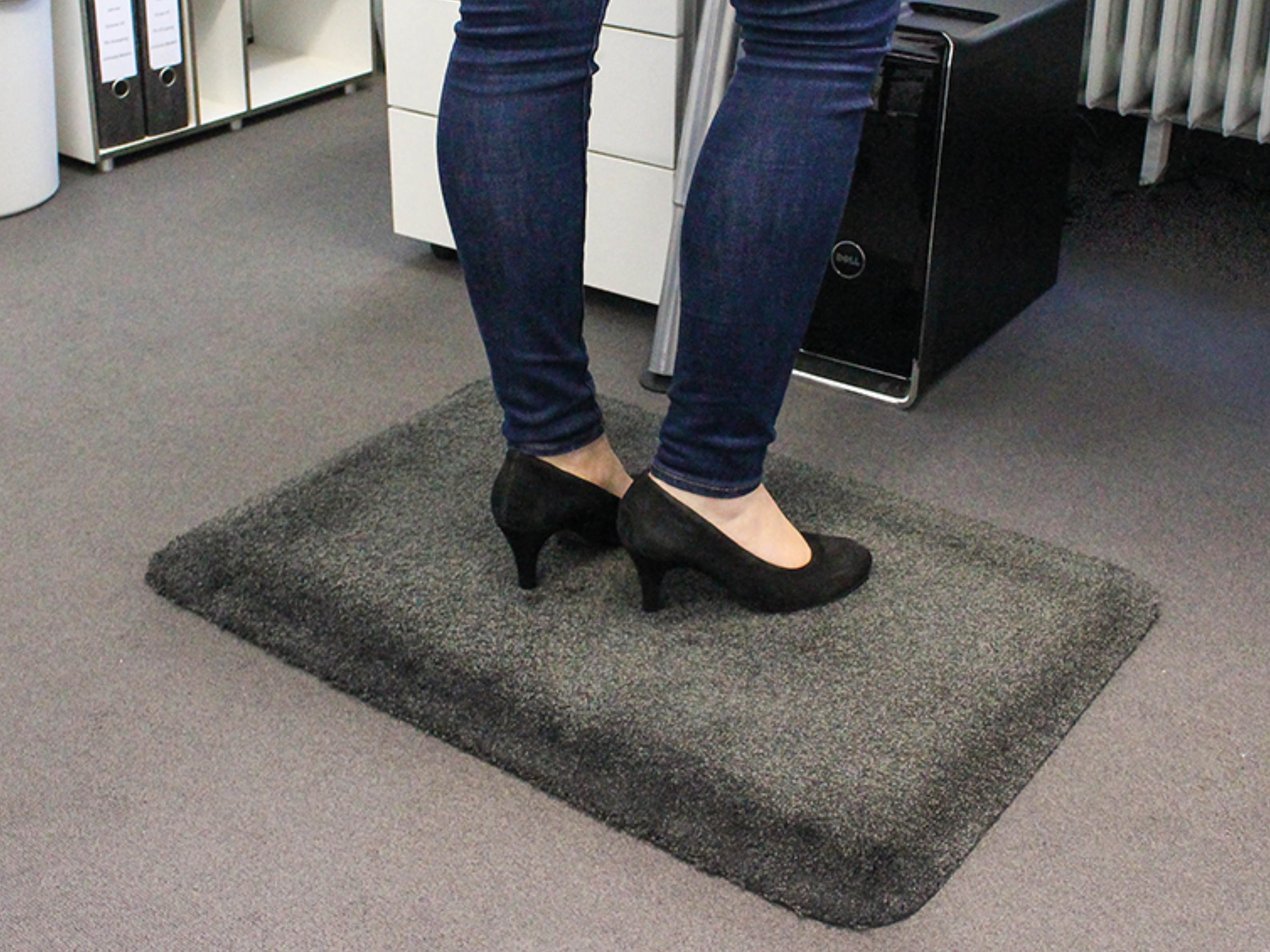 Frau mit Jeans steht auf ergonomischer Arbeitsplatzmatte mit Teppichoberfläche im Büro