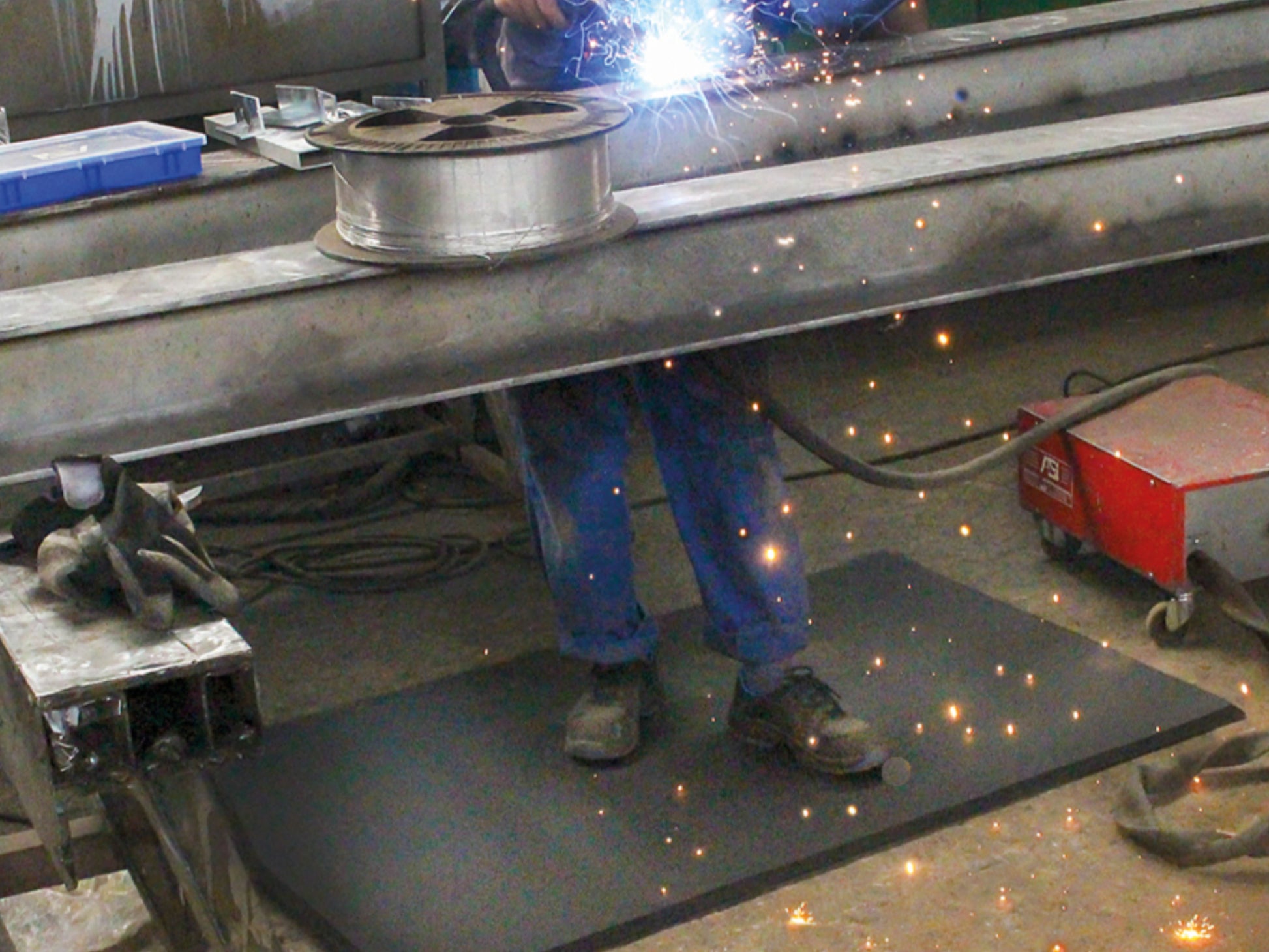 Schweißer steht auf Arbeitsplatzmatte Ergo Air während er unter Funkenflug schweißt 