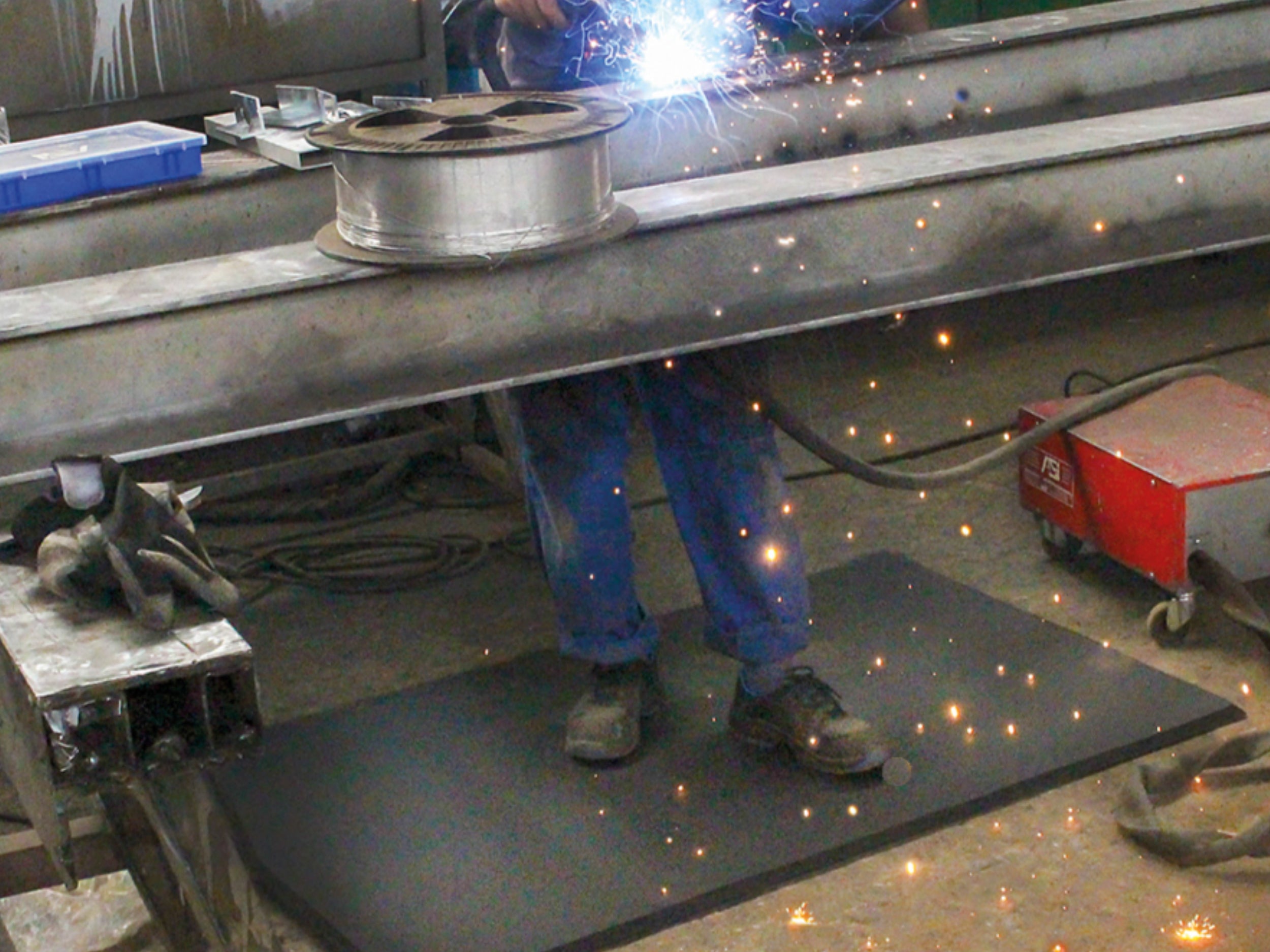 Schweißer steht auf Arbeitsplatzmatte Ergo Air während er unter Funkenflug schweißt 