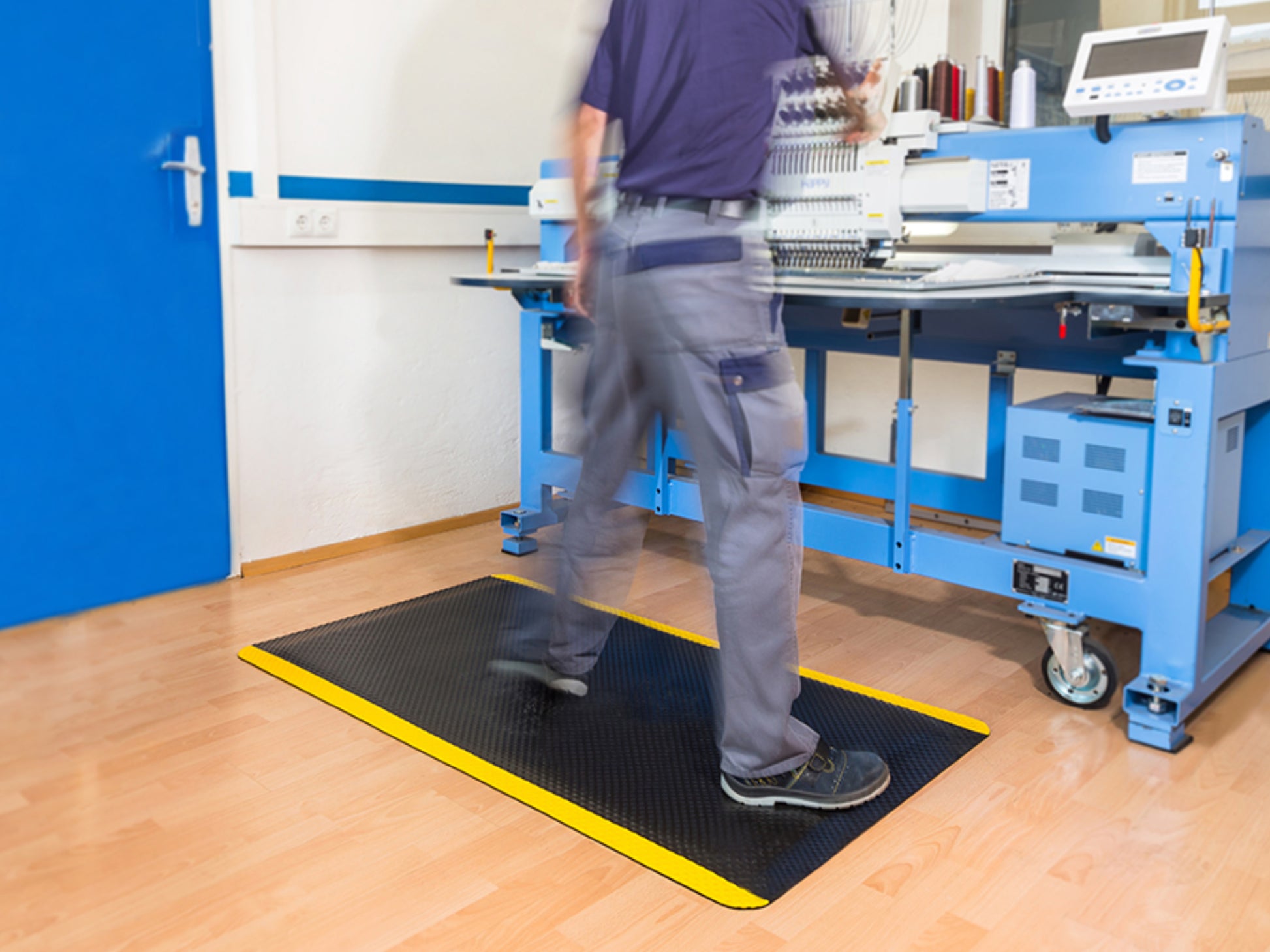 Arbeiter steht auf ergonomischer Steharbeitsplatzmatte an Montageplatz