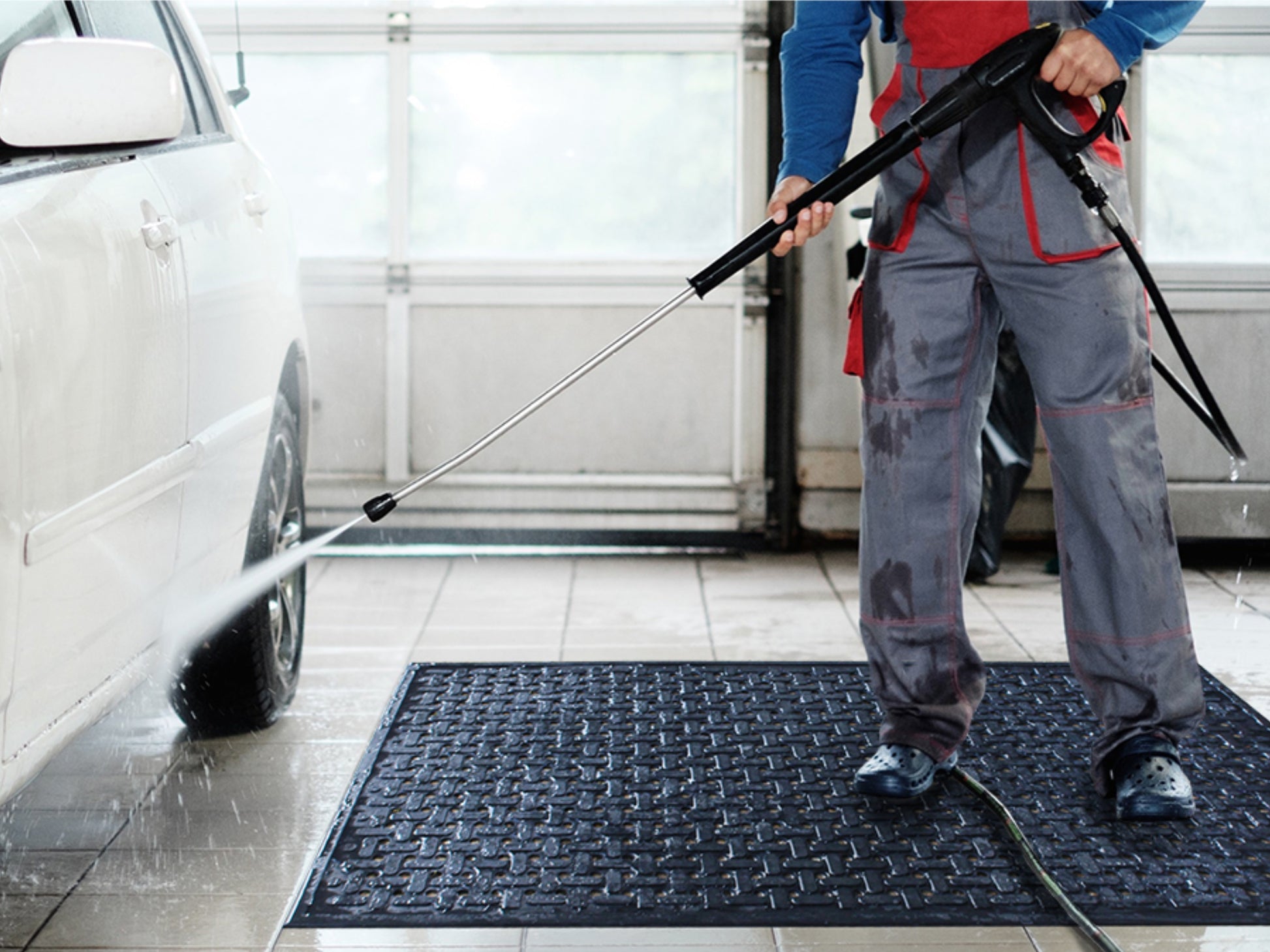 Ein Mitarbeiter reinigt ein Auto mit  einem Hochdruckreiner und steht auf der Gummi Arbeitsplatzmatte Pro Work mit Drainagelöchern 