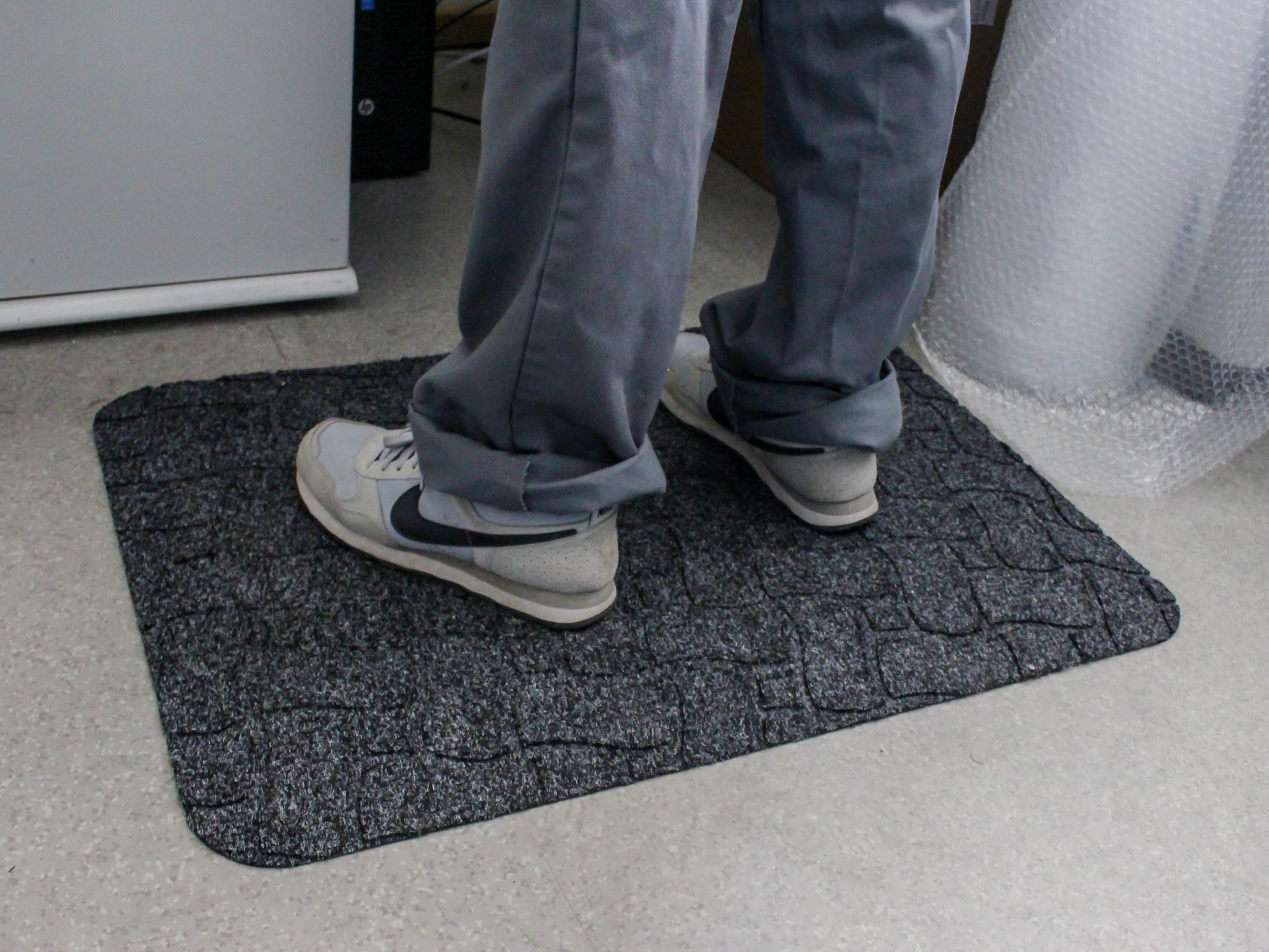 Mitarbeiter steht auf ergonomischer Arbeitsplatzmatte mit Ripsoberfläche Ergo Grip