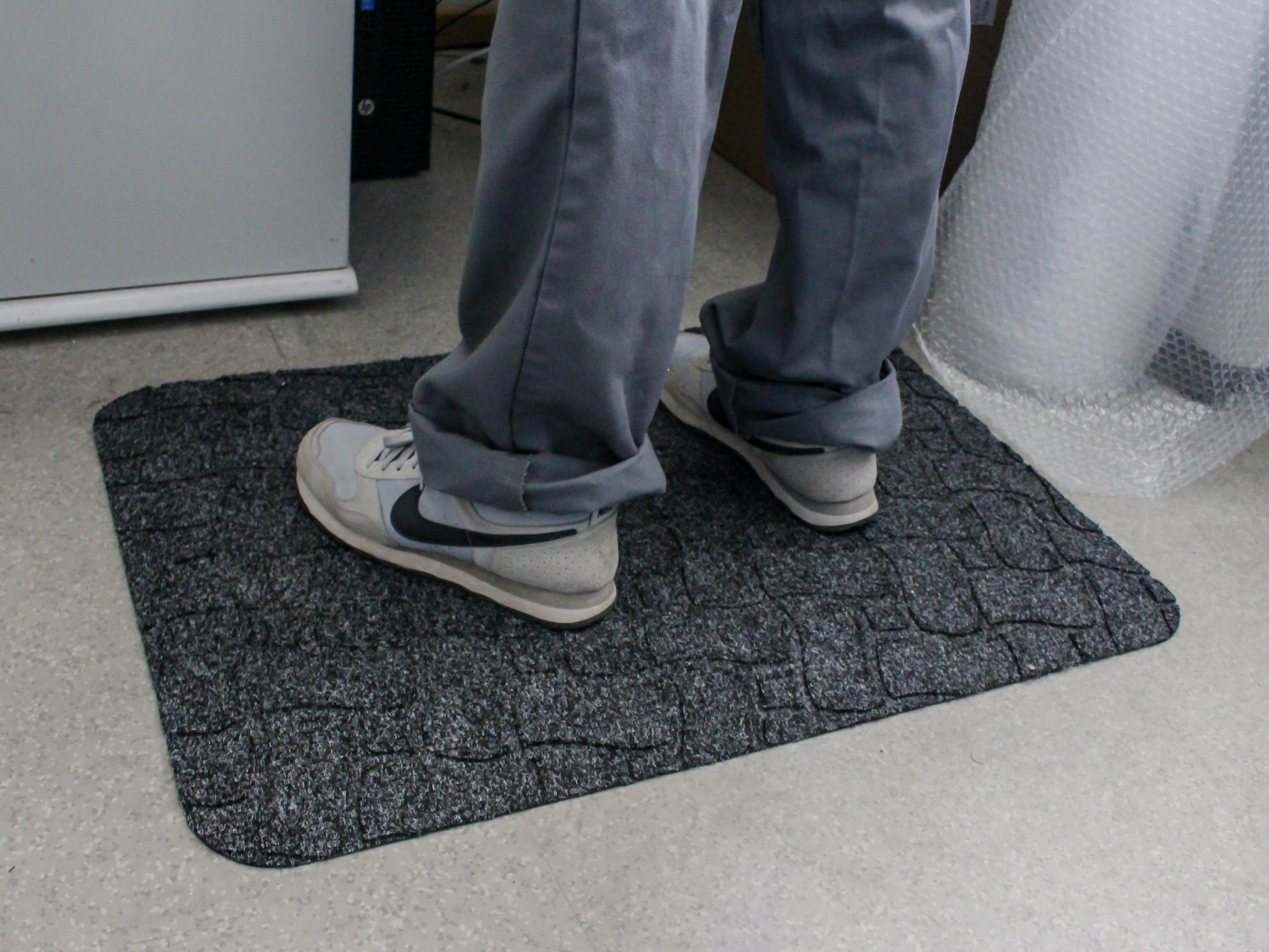 Mitarbeiter steht auf ergonomischer Arbeitsplatzmatte mit Ripsoberfläche Ergo Grip