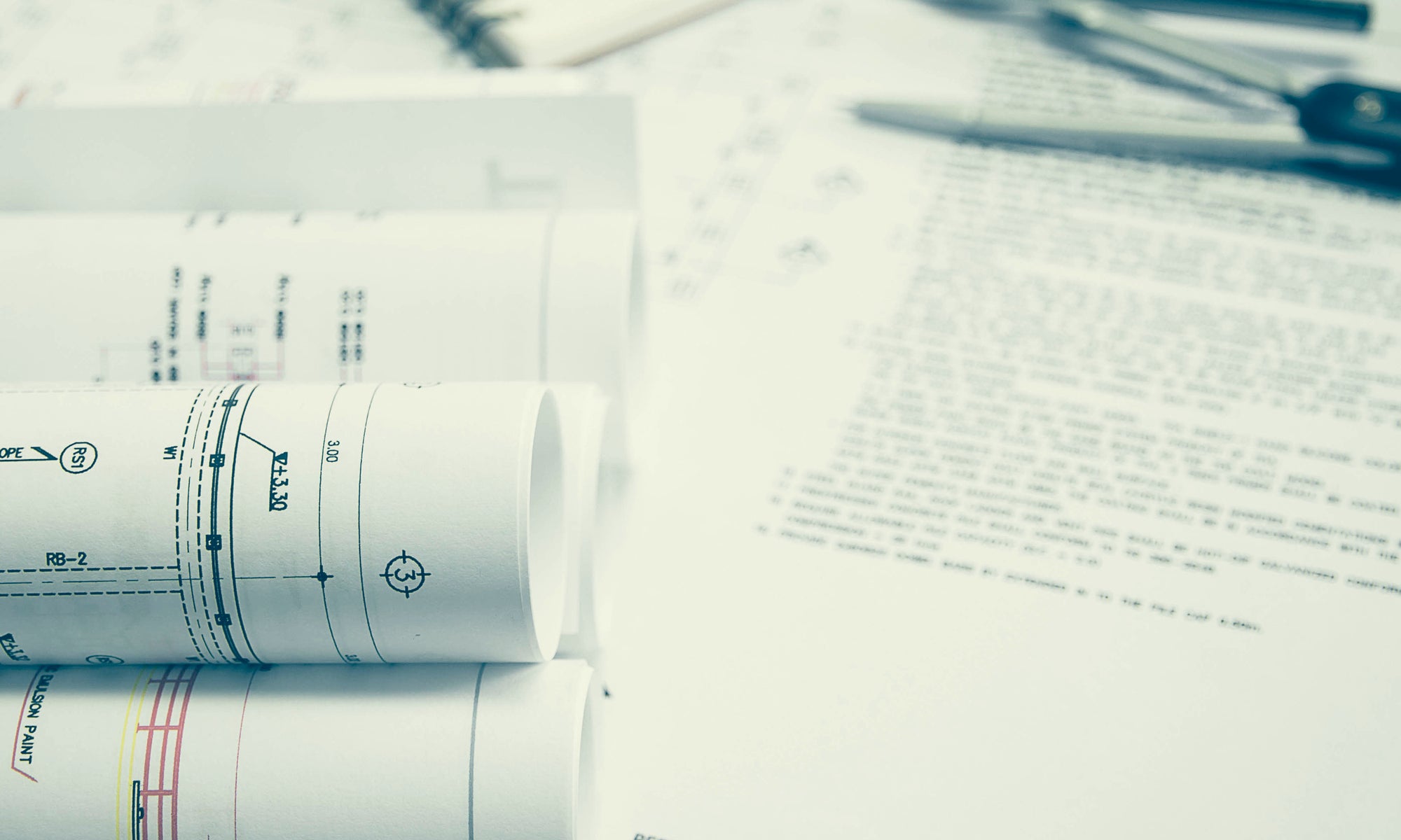 Schreibtisch gefüllt mit Bauplänen, Ausschreibungstexten und Zeichenutensilien