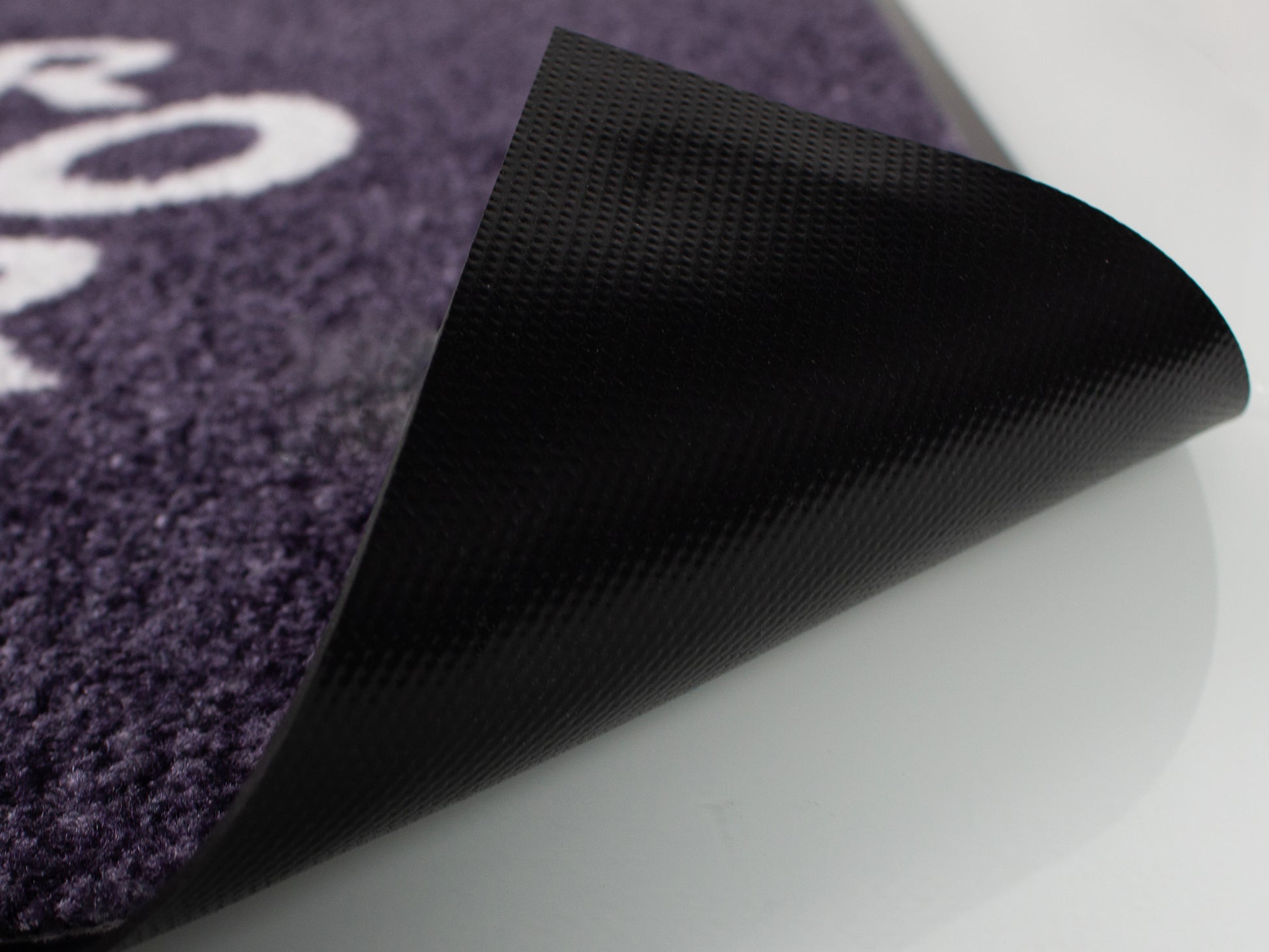 Bedruckte Fußmatte deren Ecke angehoben ist um die Unterseite zu sehen in der Detailaufnahme