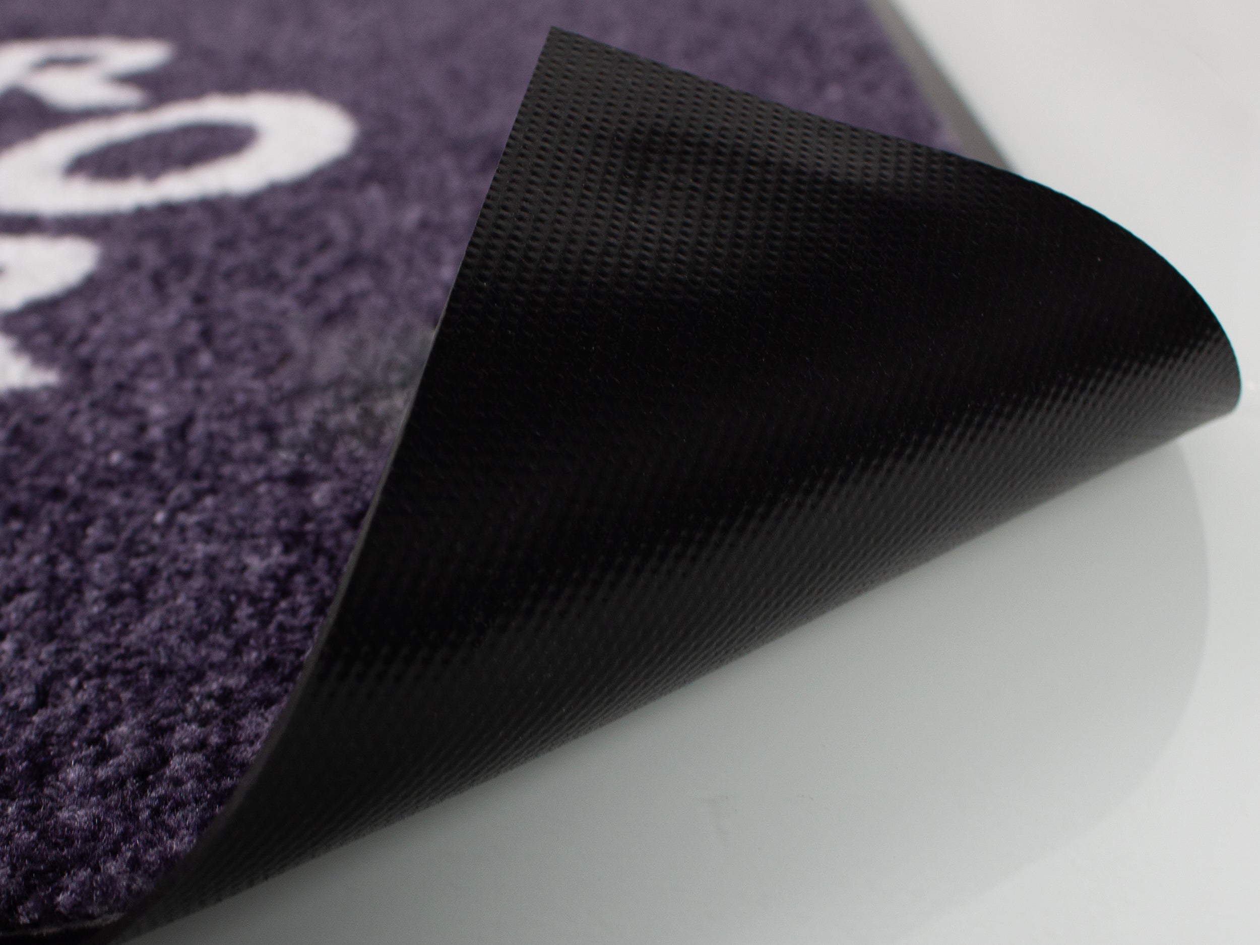 Bedruckte Fußmatte deren Ecke angehoben ist um die Unterseite zu sehen in der Detailaufnahme