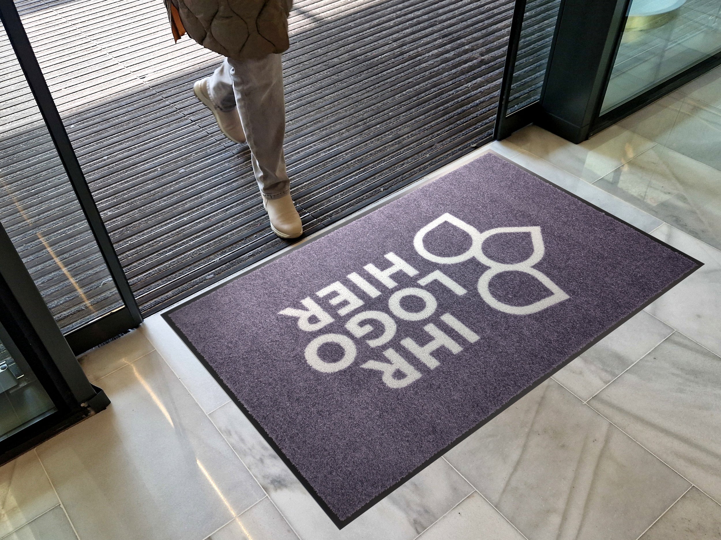 Bedruckte Fußmatte mit Ihr Logo Hier Aufdruck in einem Eingansbereich mit Schiebetüren