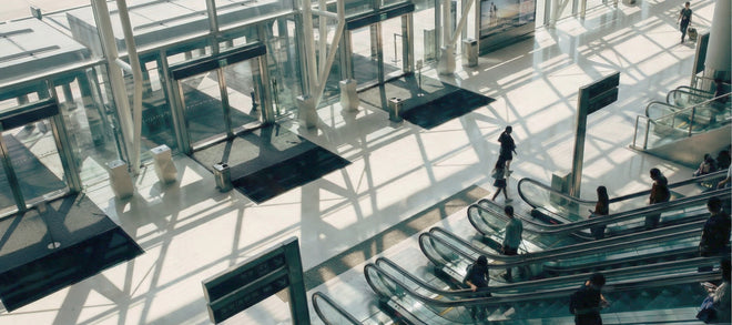 Gebäude aus Glas mit Rolltreppen und mehreren Eingangstüren mit davor liegenden Fußmatten.