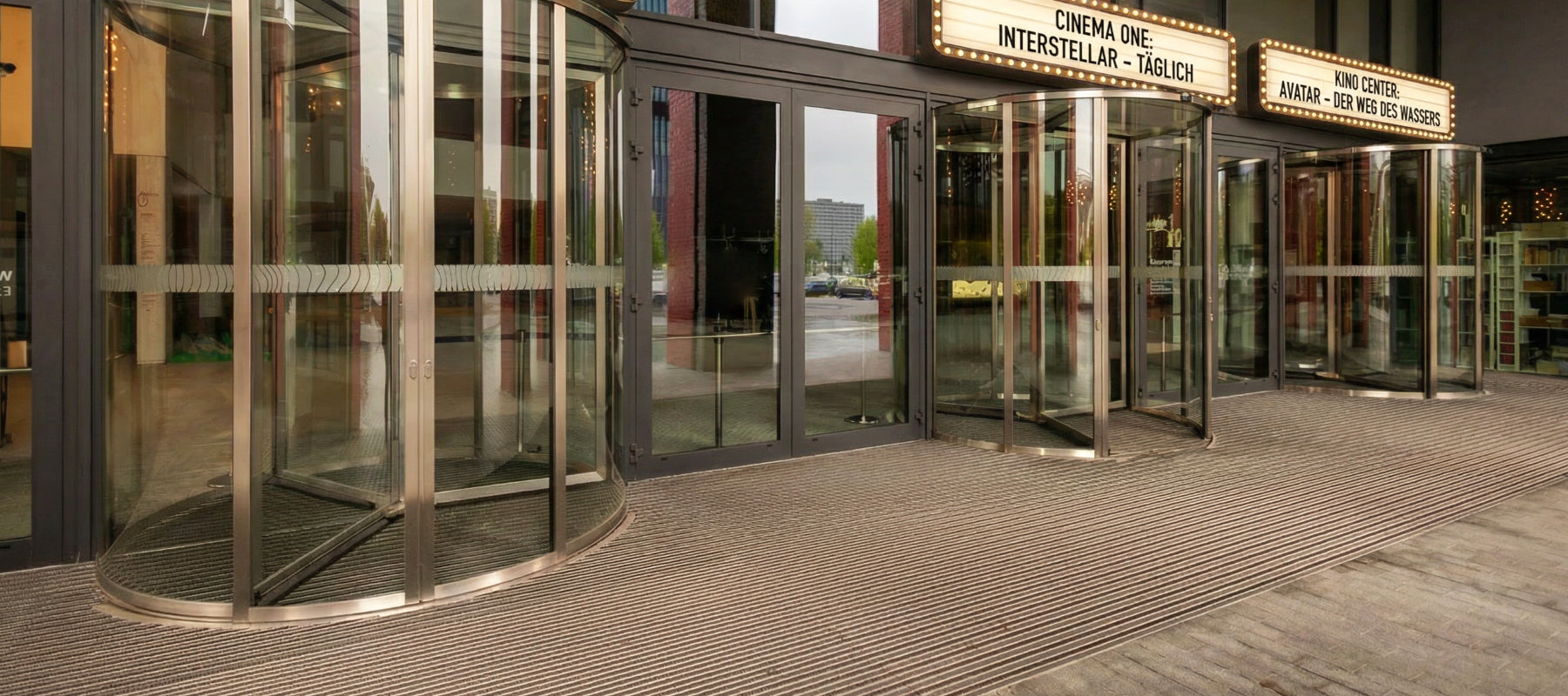 Eingang eines Kinos mit Glasdrehtüren und Fußmatten vor der Tür