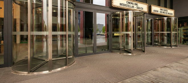 Eingang eines Kinos mit Glasdrehtüren und Fußmatten vor der Tür