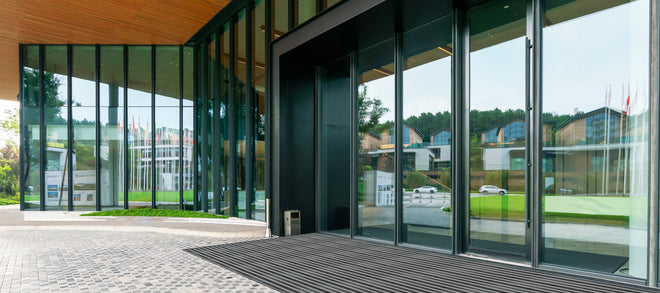 Glasfront von Gebäude mit Aluminiumprofilmatte im Steinboden  vor Eingangstür eingelassen