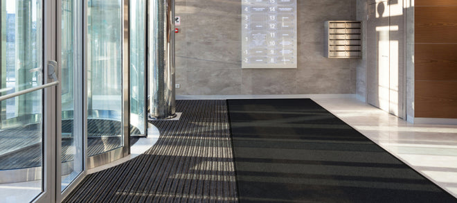 Eingangsfoyer mit Steinboden und Fußmatten aus Teppich und Aluminium hinter einer Drehtür