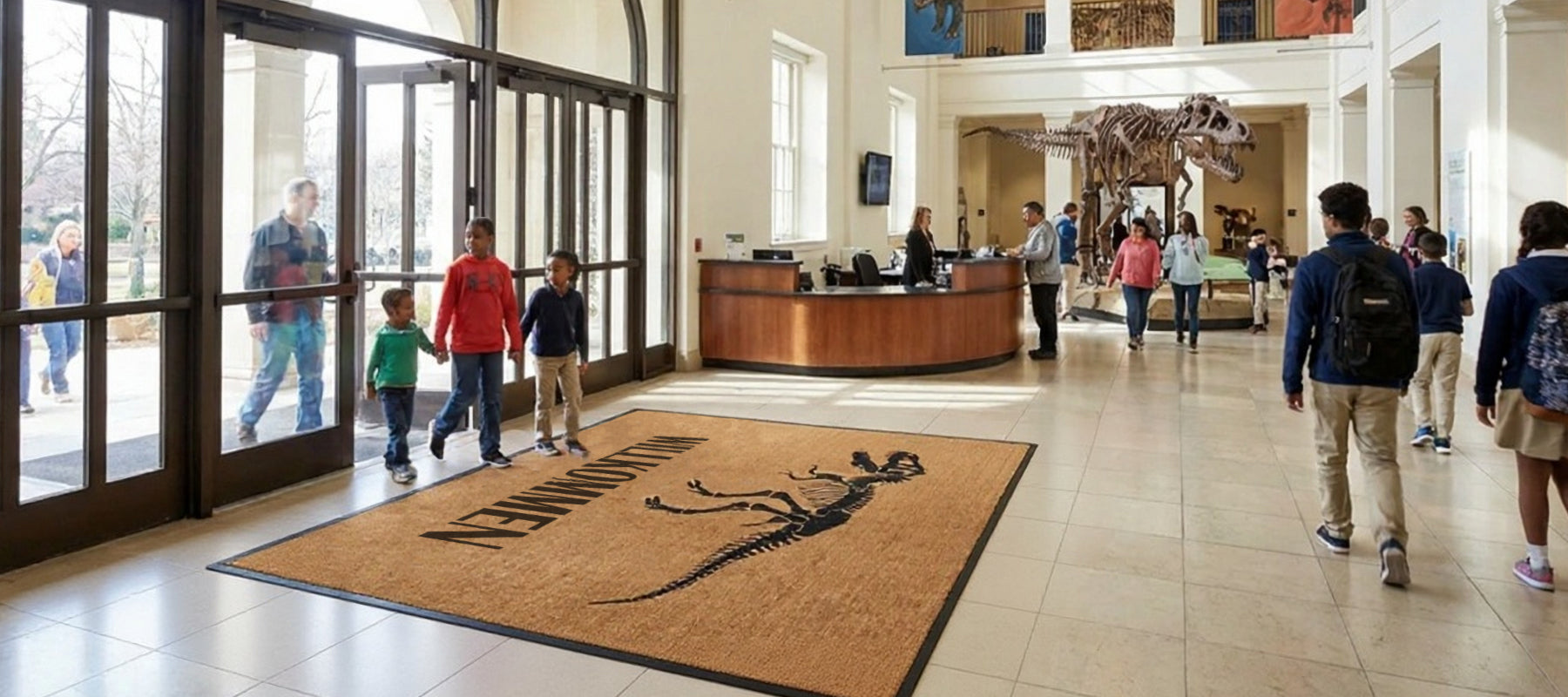 Eingangshalle von einem Museum mit Besuchern, einer Dinosaurierfußmatte vor der Tür und einem Dinosaurierskelett