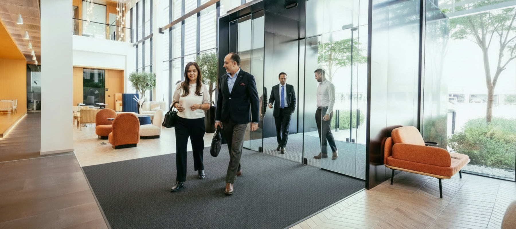 Großzügiger Eingangsbereich mit Glasfront. Personen in Businesskleidung laufen über Eingangsteppich.