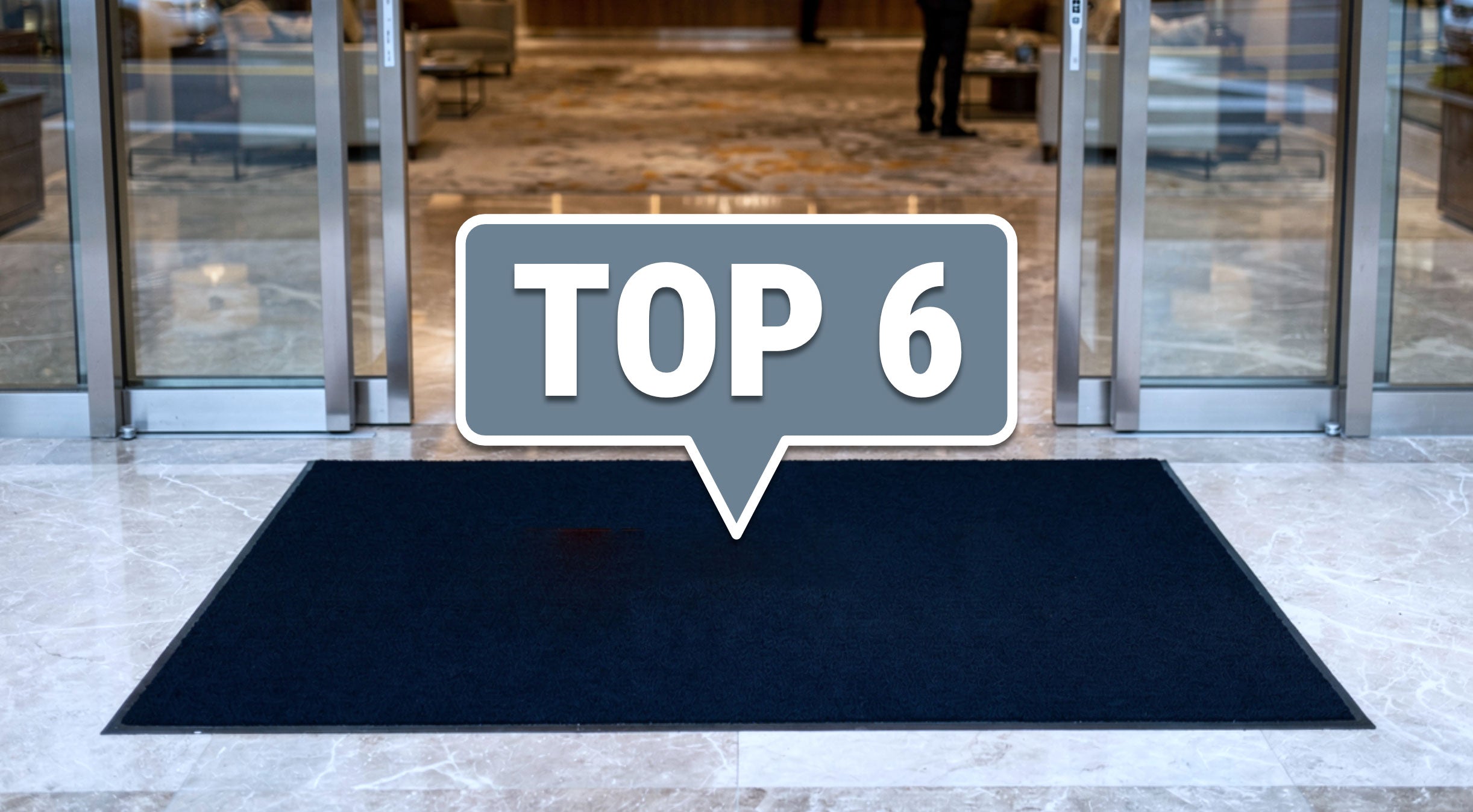Schmutzfangmatte in schwarz liegt vor einer Glastür eines Foyers. Top 6 steht in einer Sprechblase darüber.