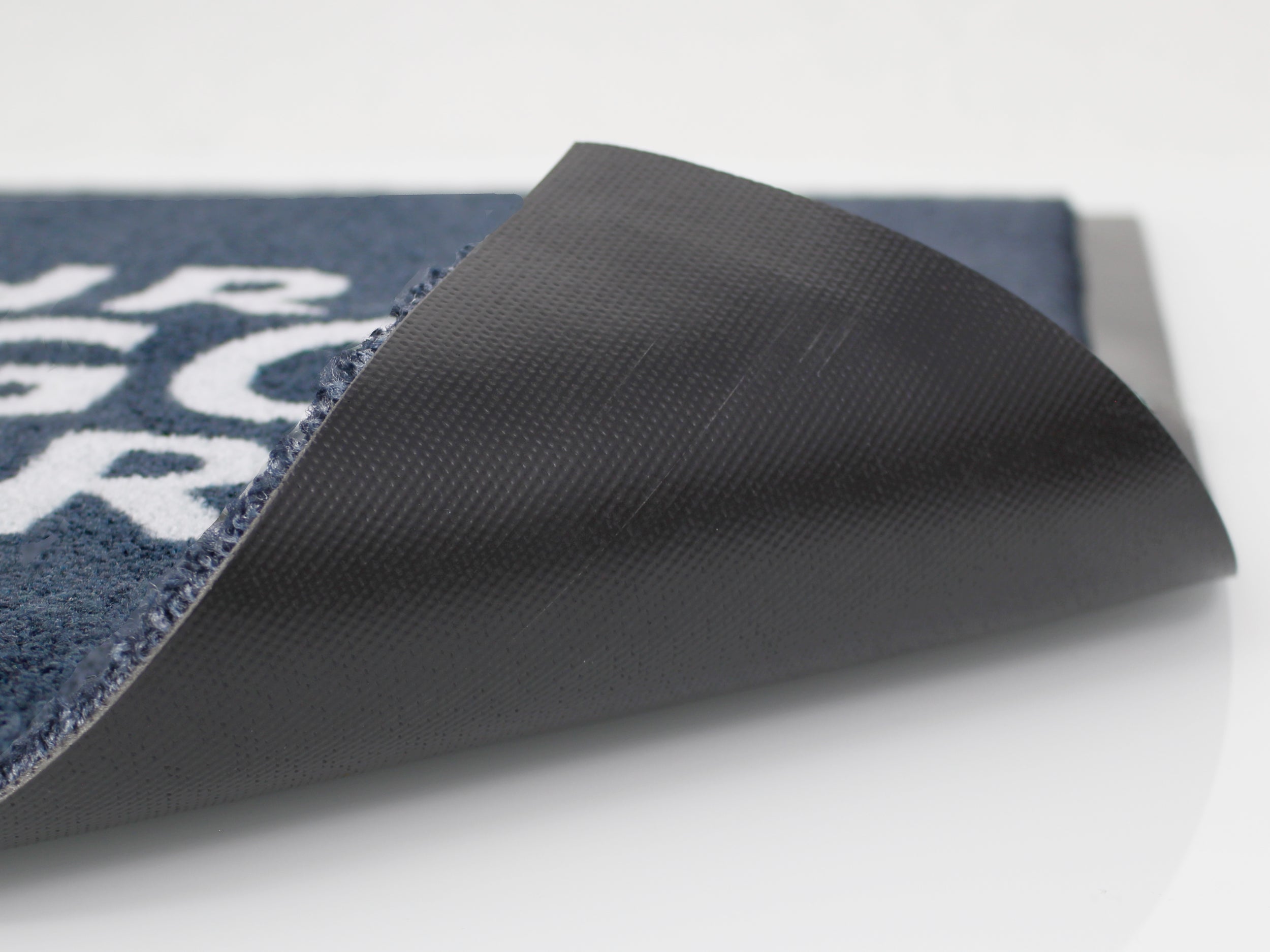 Umgeklappter, schwarzer PVC Rücken einer grauen Logomatte mit weißer Schrift 