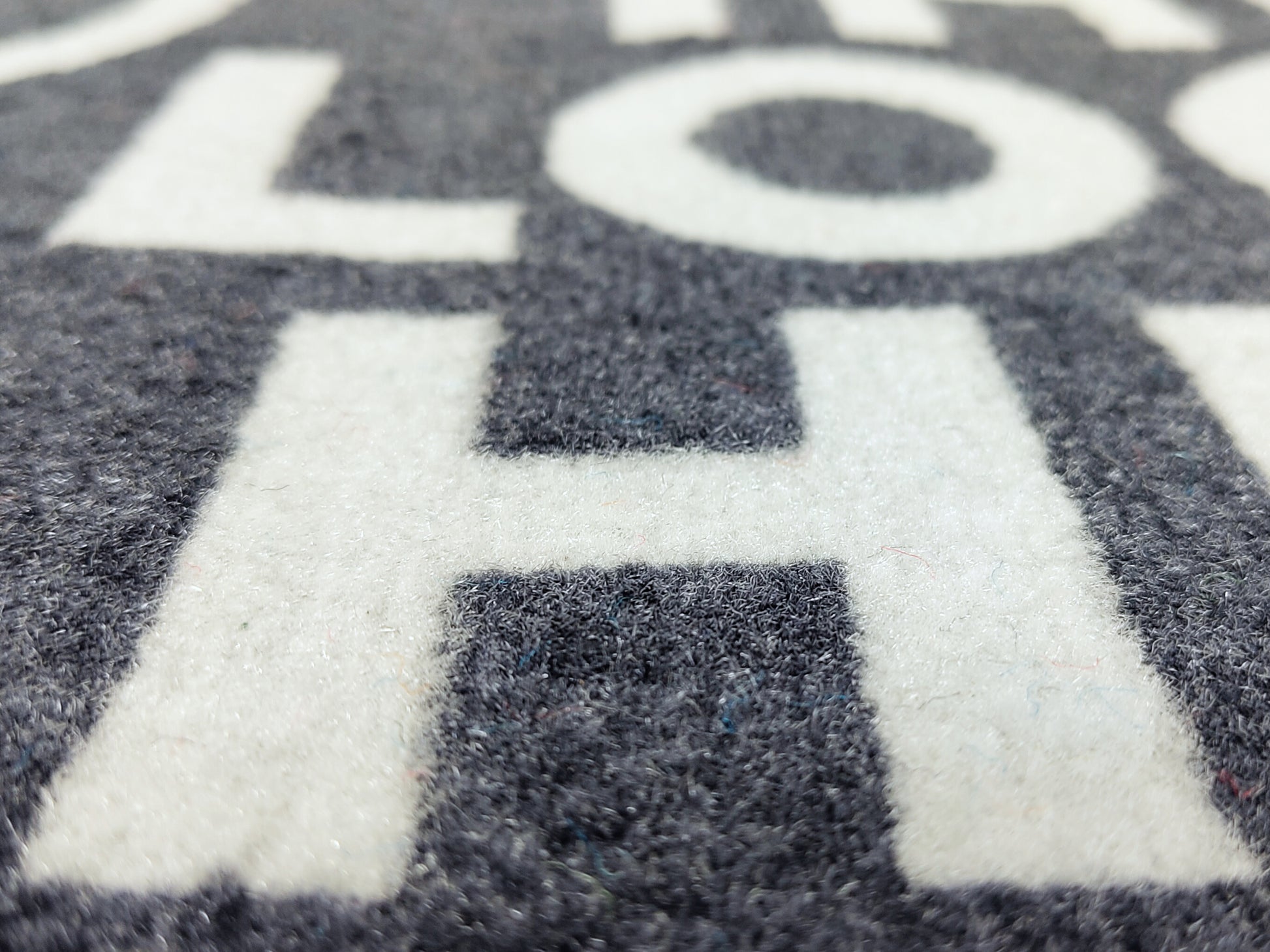 Nahaufnahme des weißen Schriftzugs einer fotorealistischen, grauen Fußmatte