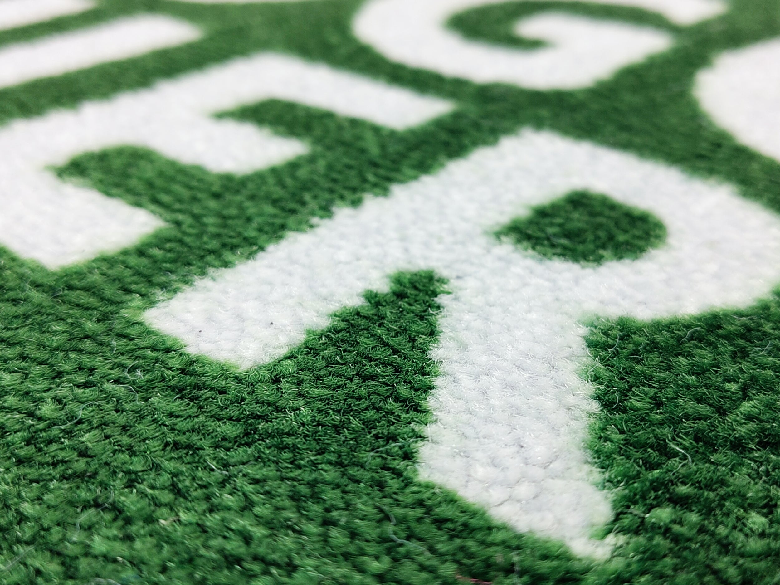 Nachaufnahme des Druckbildes einer grünen Logomatte mit weißer Schrift