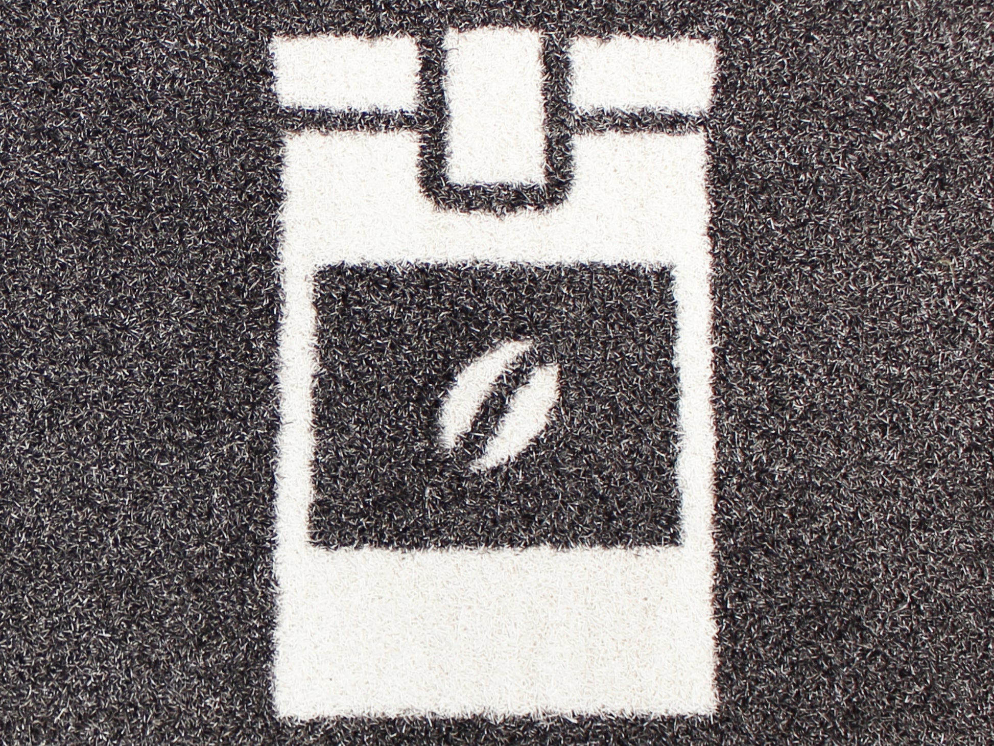 Eine Nahaufnahme, von einer braunen, bedruckten Matte, die einen Kaffeebehälter mit einer Kaffeebohne anzeigt.