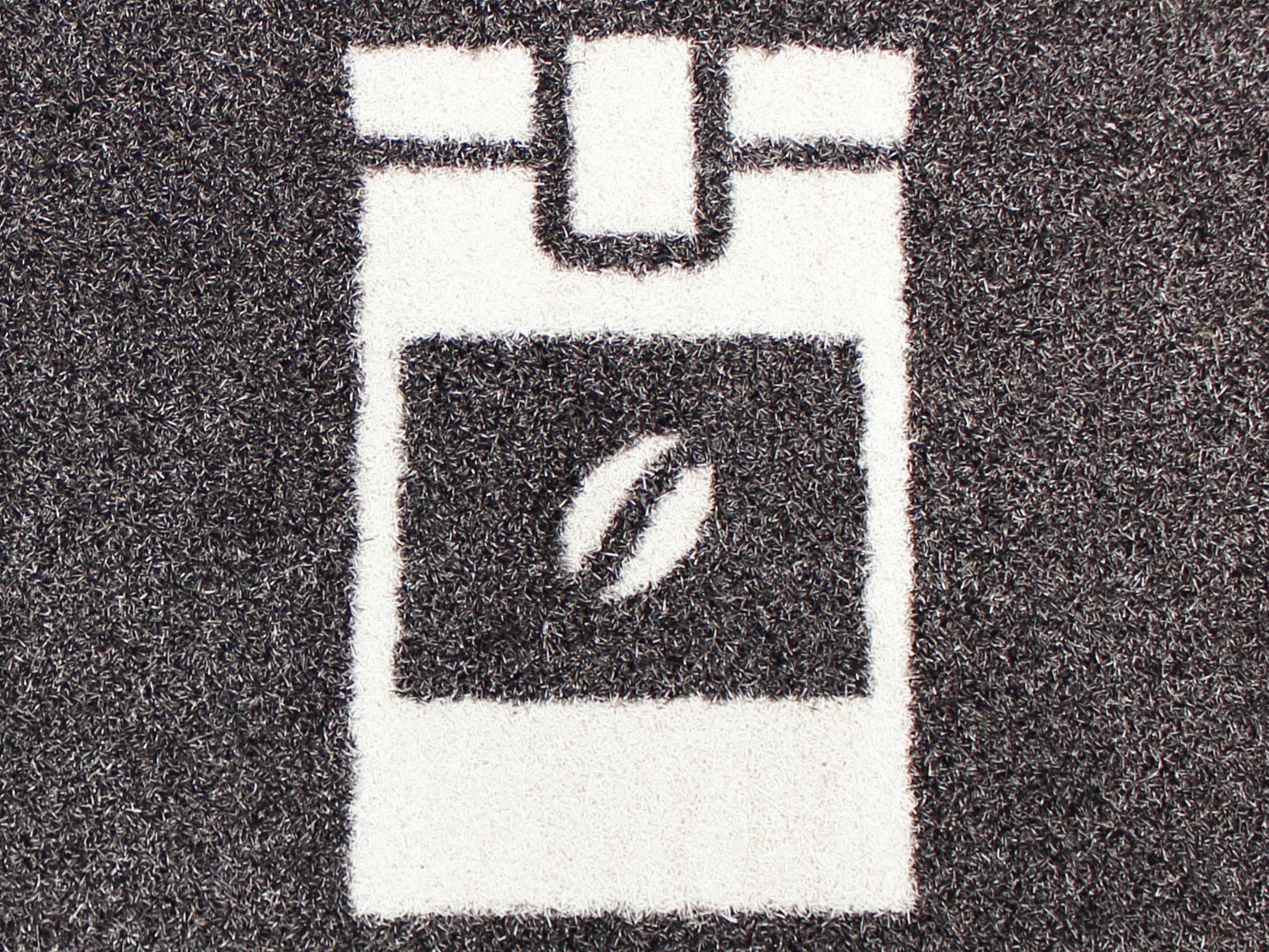 Eine Nahaufnahme, von einer braunen, bedruckten Matte, die einen Kaffeebehälter mit einer Kaffeebohne anzeigt.