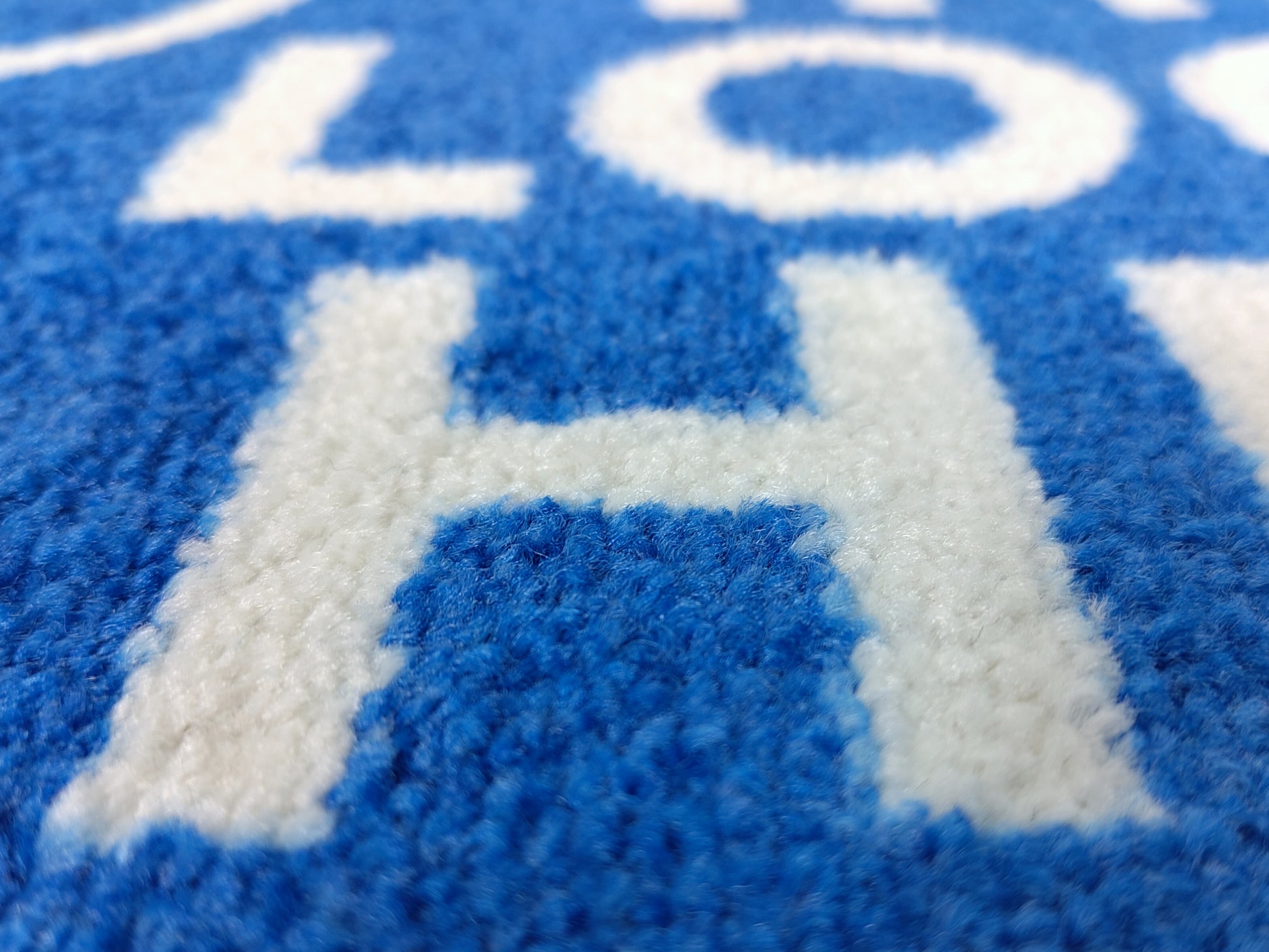 Nahaufnahme des Druckbildes einer blauen, kurzfristig verfügbaren Logomatte mit weißer Schrift