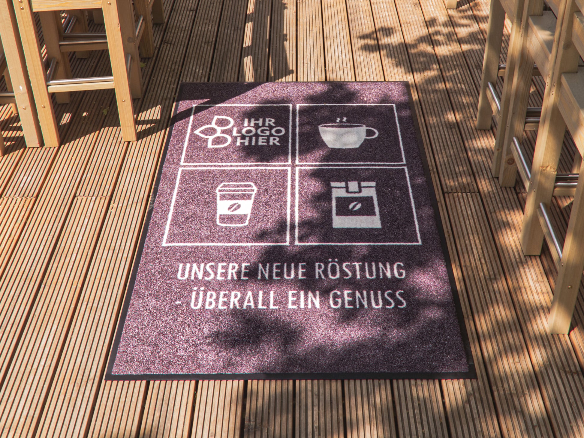 Eine rötlich melierte Matte die auf einem Balkon liegt; mit einer Kaffeetasse, Becher und Kaffeeaufbewahrung fein säuberlich bedruckt. 