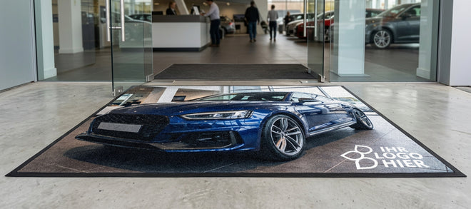 Große Fußmatte liegt im Eingang eines Autohauses und ist mit fotorealistischem Motiv eines blauen Autos bedruckt.