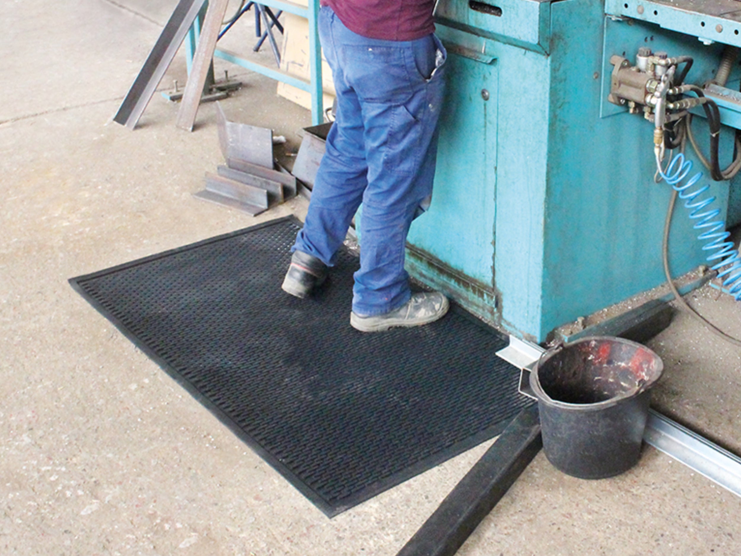 Arbeiter steht mit Sicherheitsschuhen und Handwerkerhose auf einer Arbeitsplatzmatte