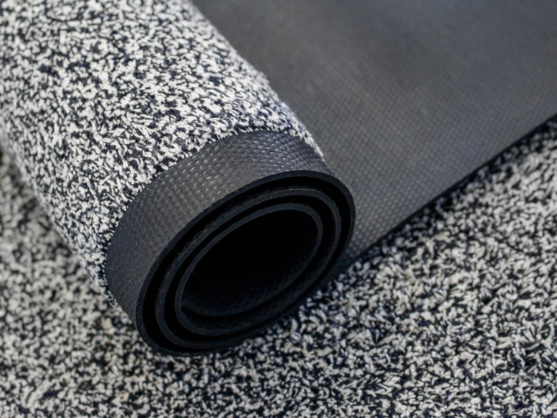 Aufgerollte Schmutzfangmatte mit weiß-schwarzer Melierung und sichtbarer Rückseite