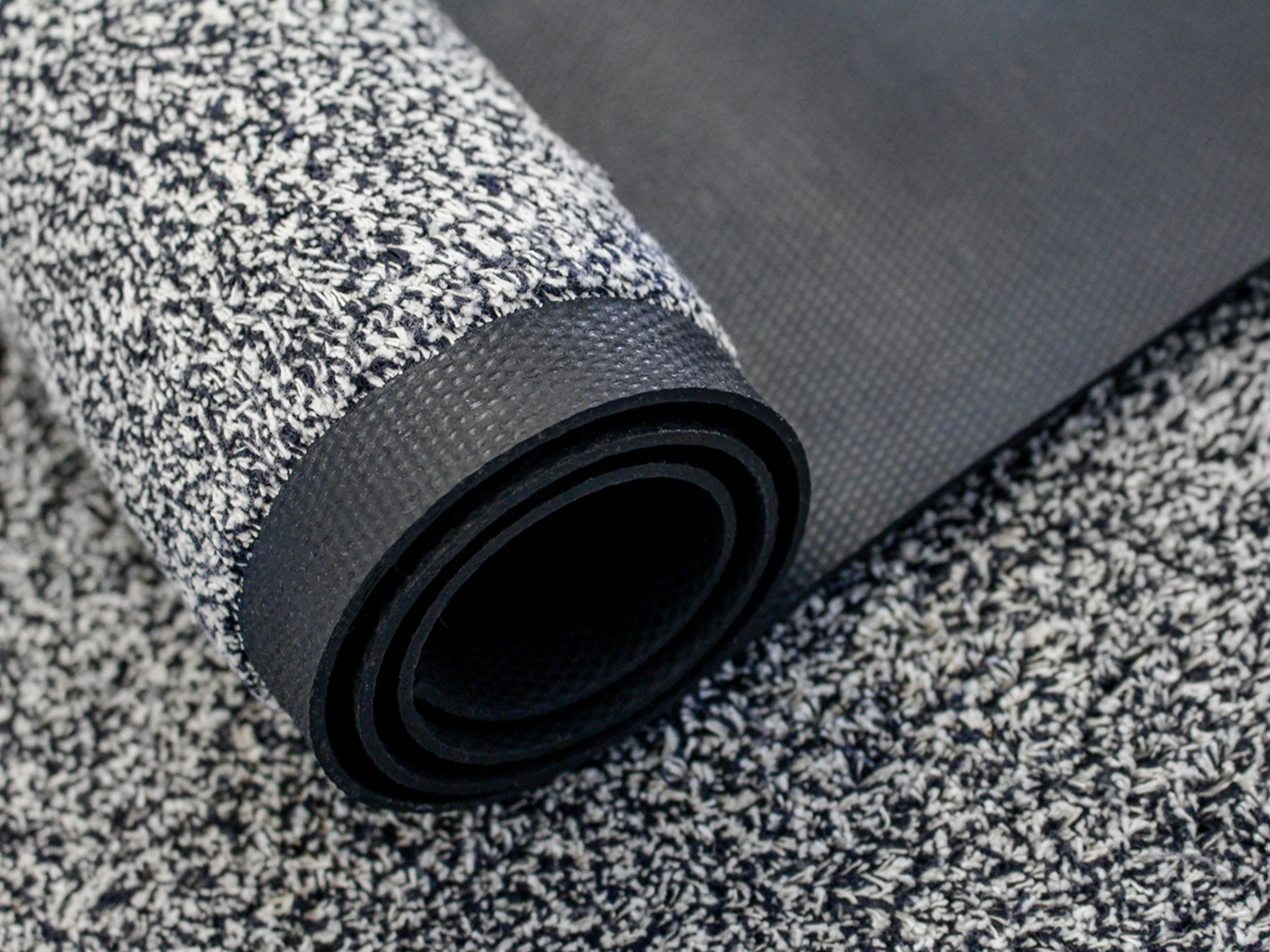 Aufgerollte Schmutzfangmatte mit weiß-schwarzer Melierung und sichtbarer Rückseite