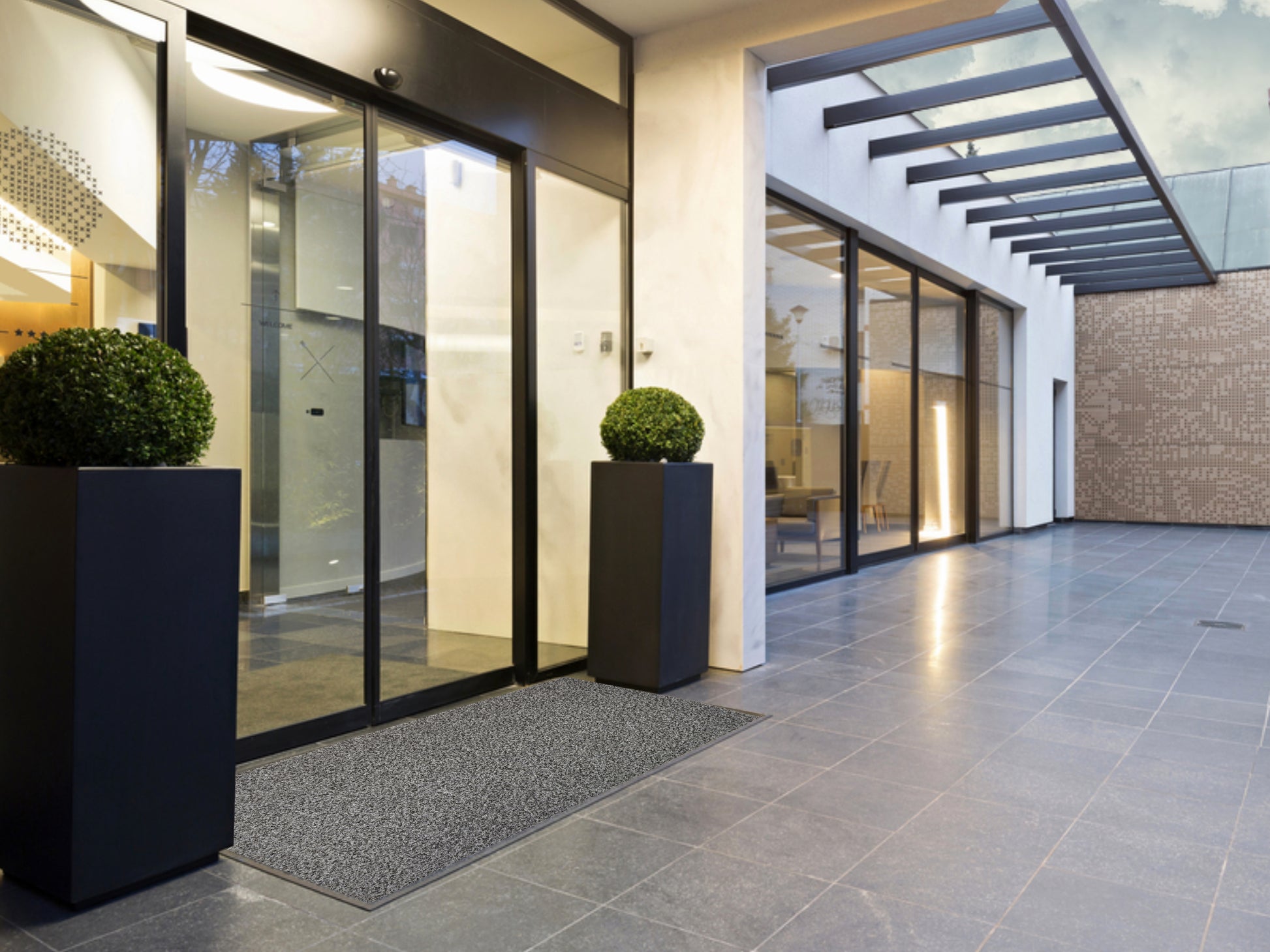 Graue Schmutzfangmatte liegt draußen vor verglasten Eingangsbereich mit elektrischer Schiebetür