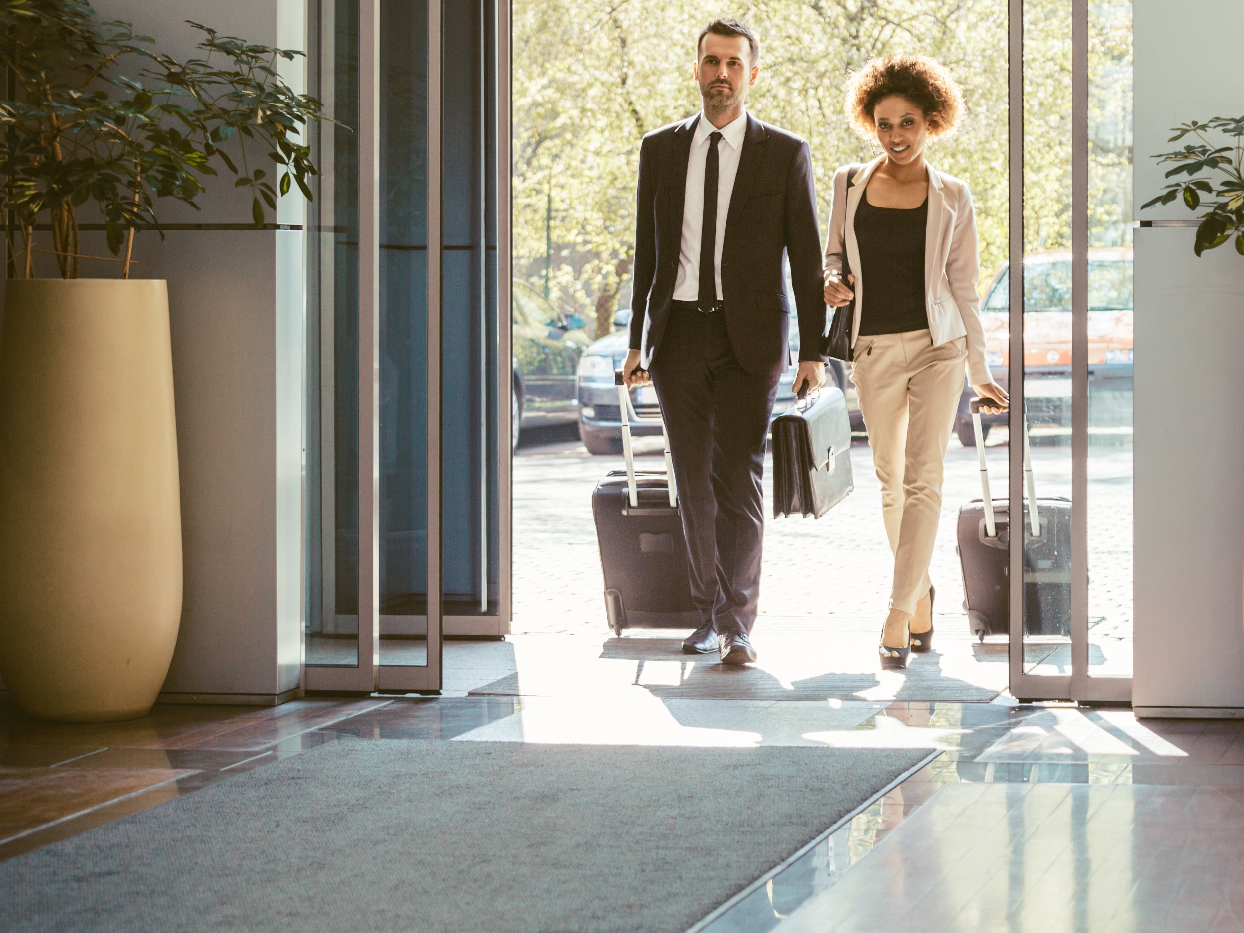 Zwei Reisende mit Koffern laufen über eine graue Schmutzfangmatte im Eingang einer Lobby