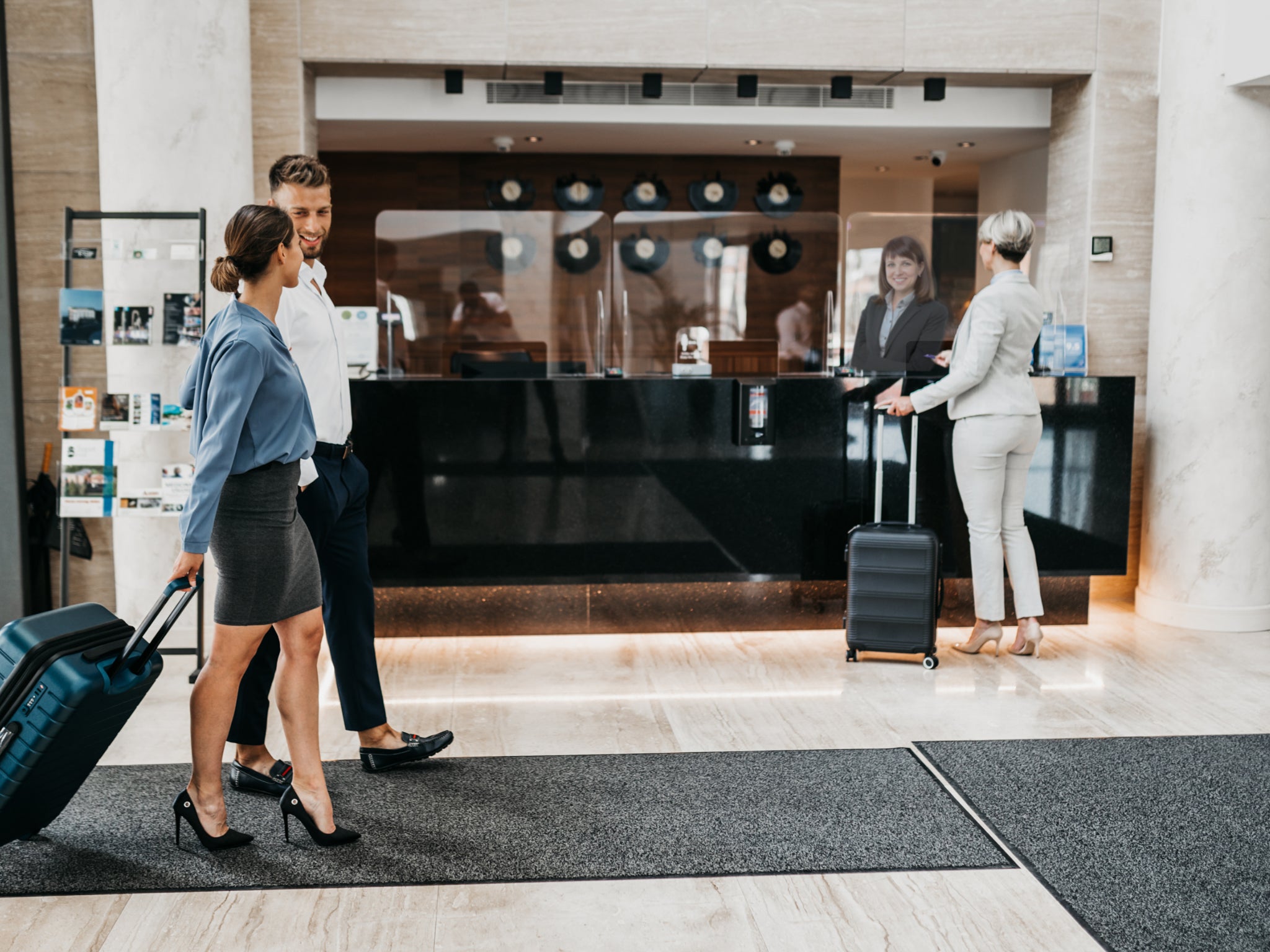 Graue Schmutzfangmatte liegt in der Lobby eines Hotels, im Gespräch befindende Reisende laufen über die Matte