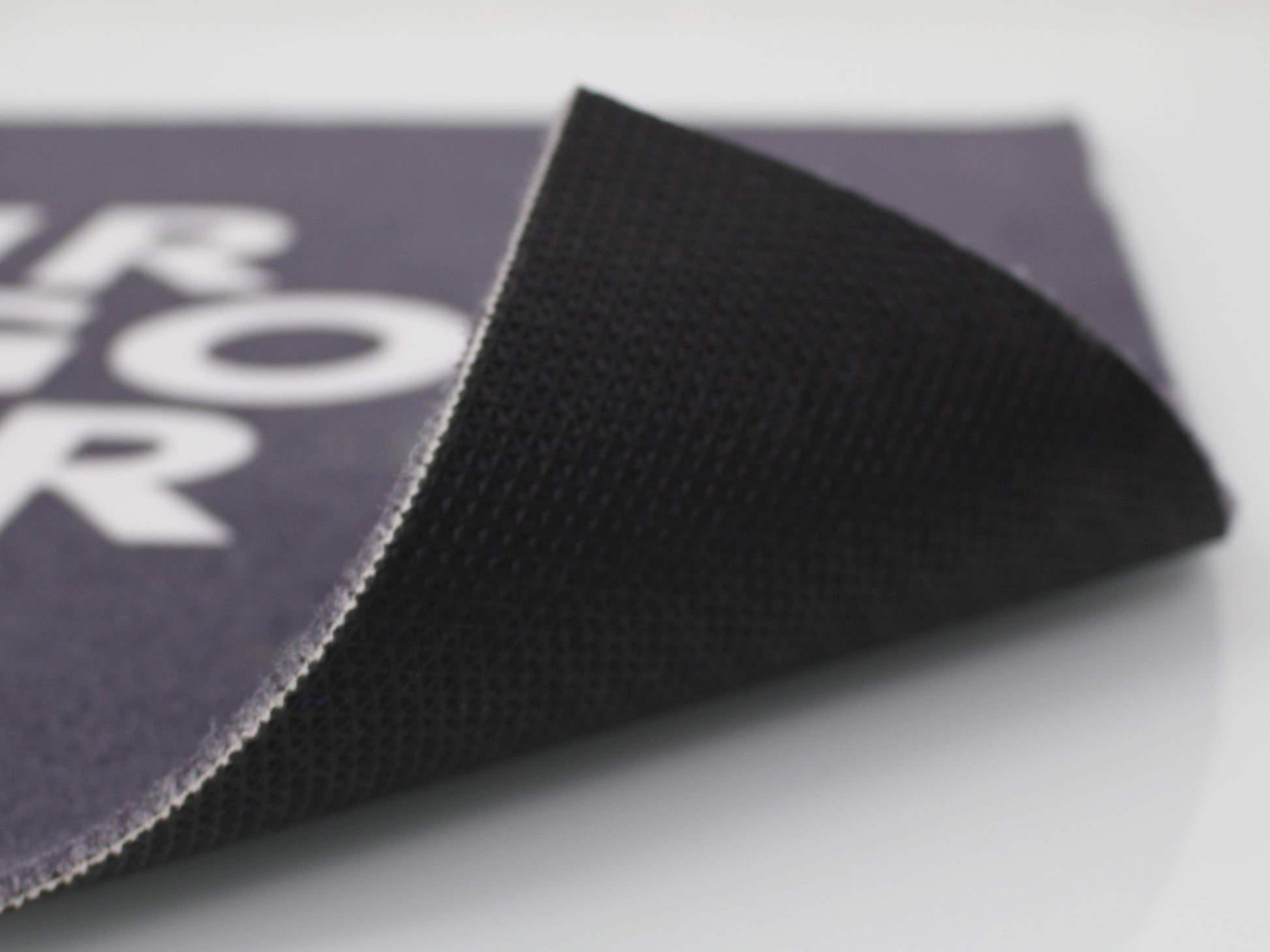 Umgeklappte Ecke einer grauen Werbematte mit weißer Schrift ohne Rand mit schwarzen PVC-Rücken