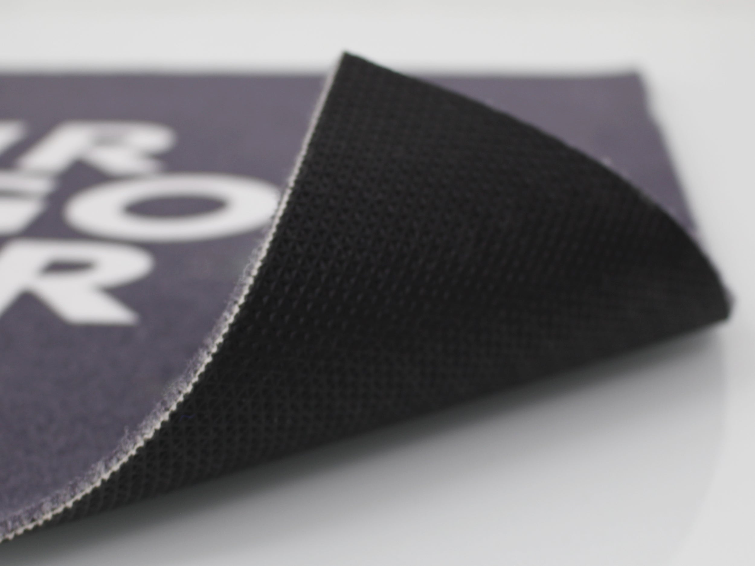 Umgeklappte Ecke einer grauen Werbematte mit weißer Schrift ohne Rand mit schwarzen PVC-Rücken