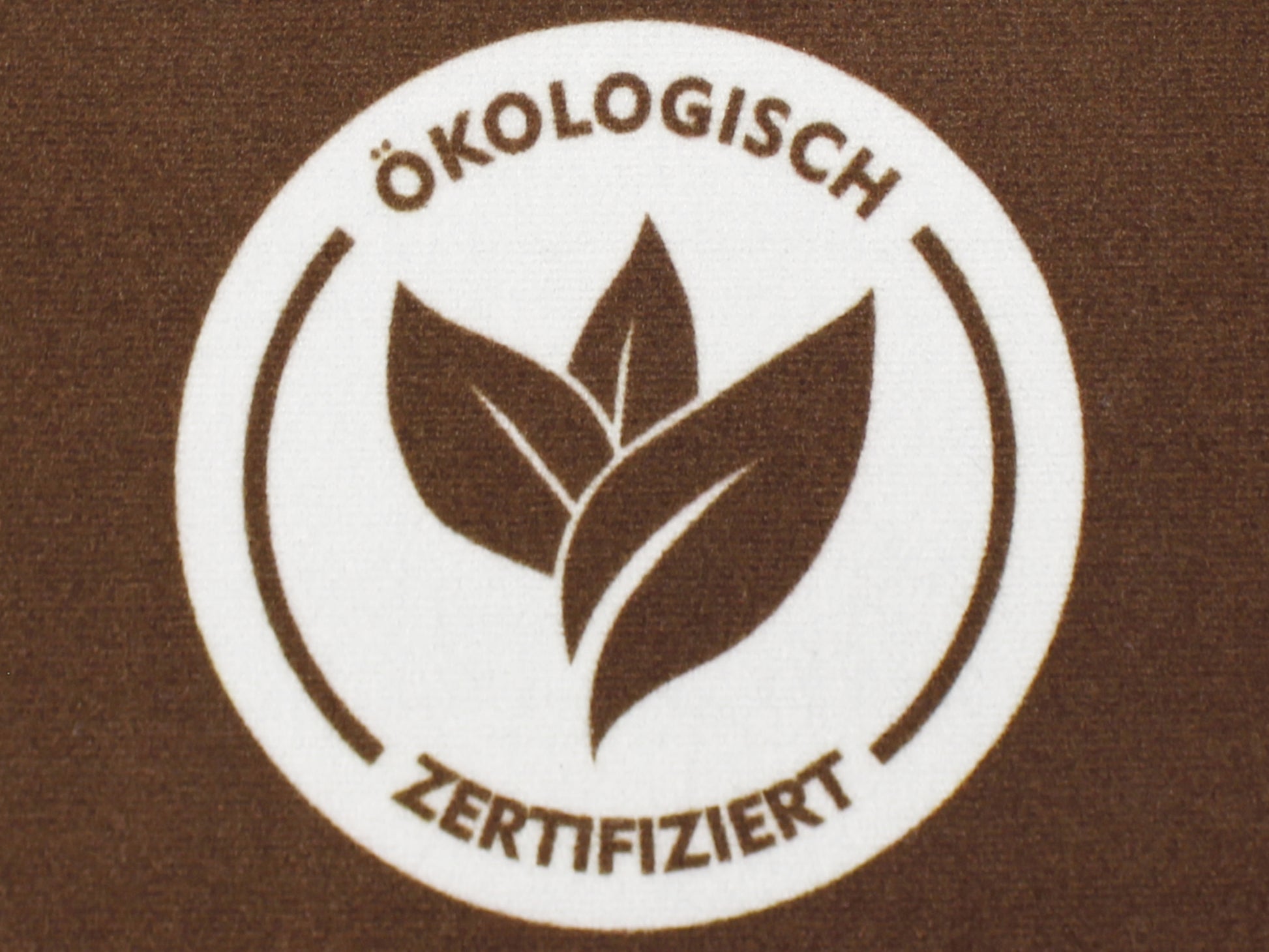 Nahaufnahme des Druckbilds einer braunen Werbematte mit einem Badge zum Thema: Ökologisch zertifiziert